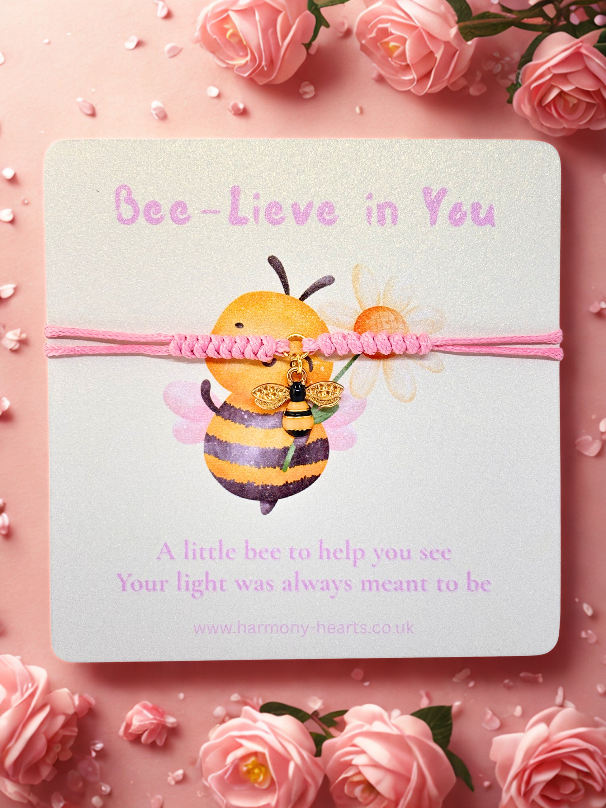 Pink cord bracelet with bee charm presented on a branded Harmony Hearts card with a bee illustration and pink ribbon on a pink background with flowers