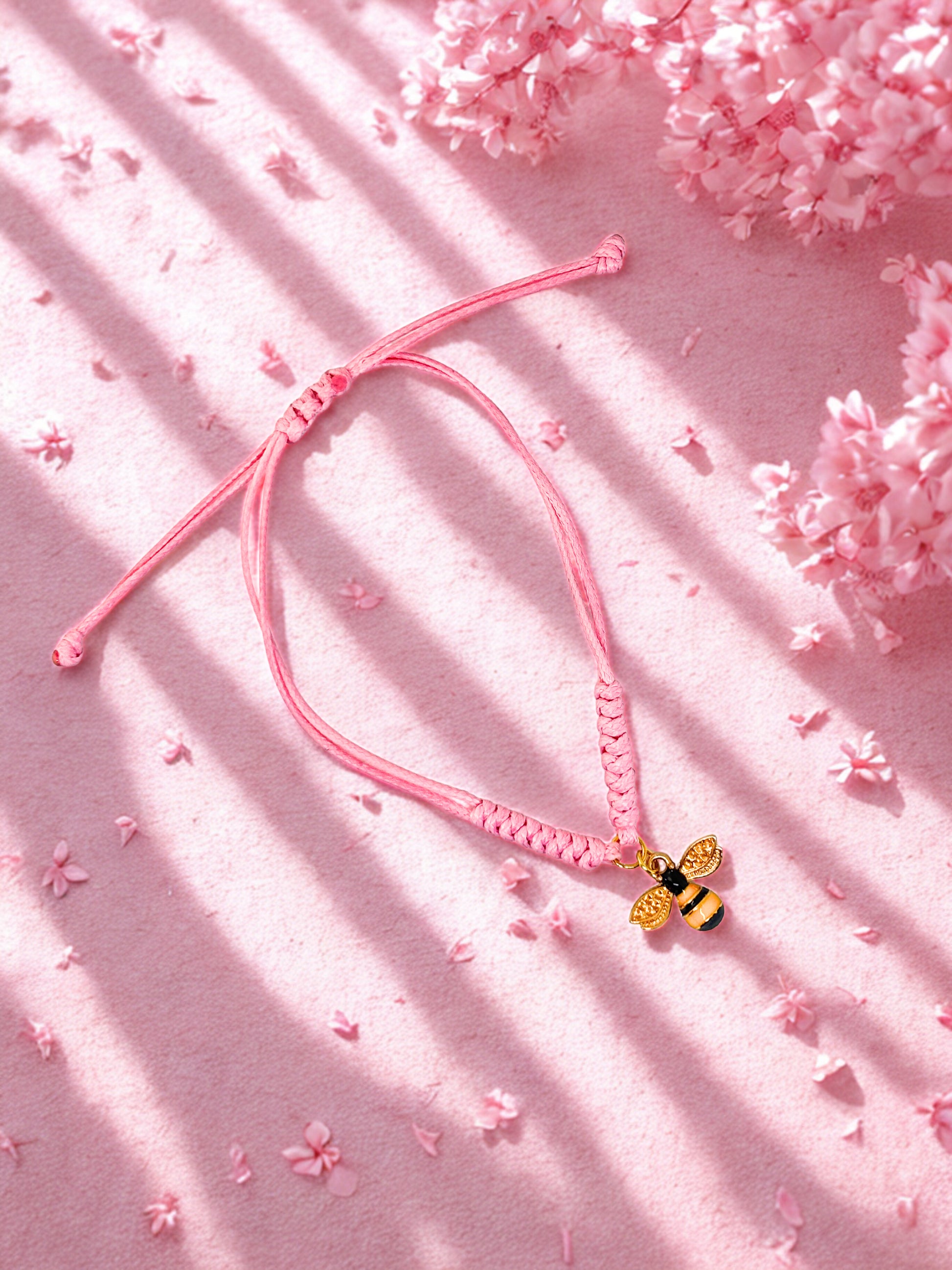 Pink cord bracelet with a bee charm on a pink background with cherry blossoms