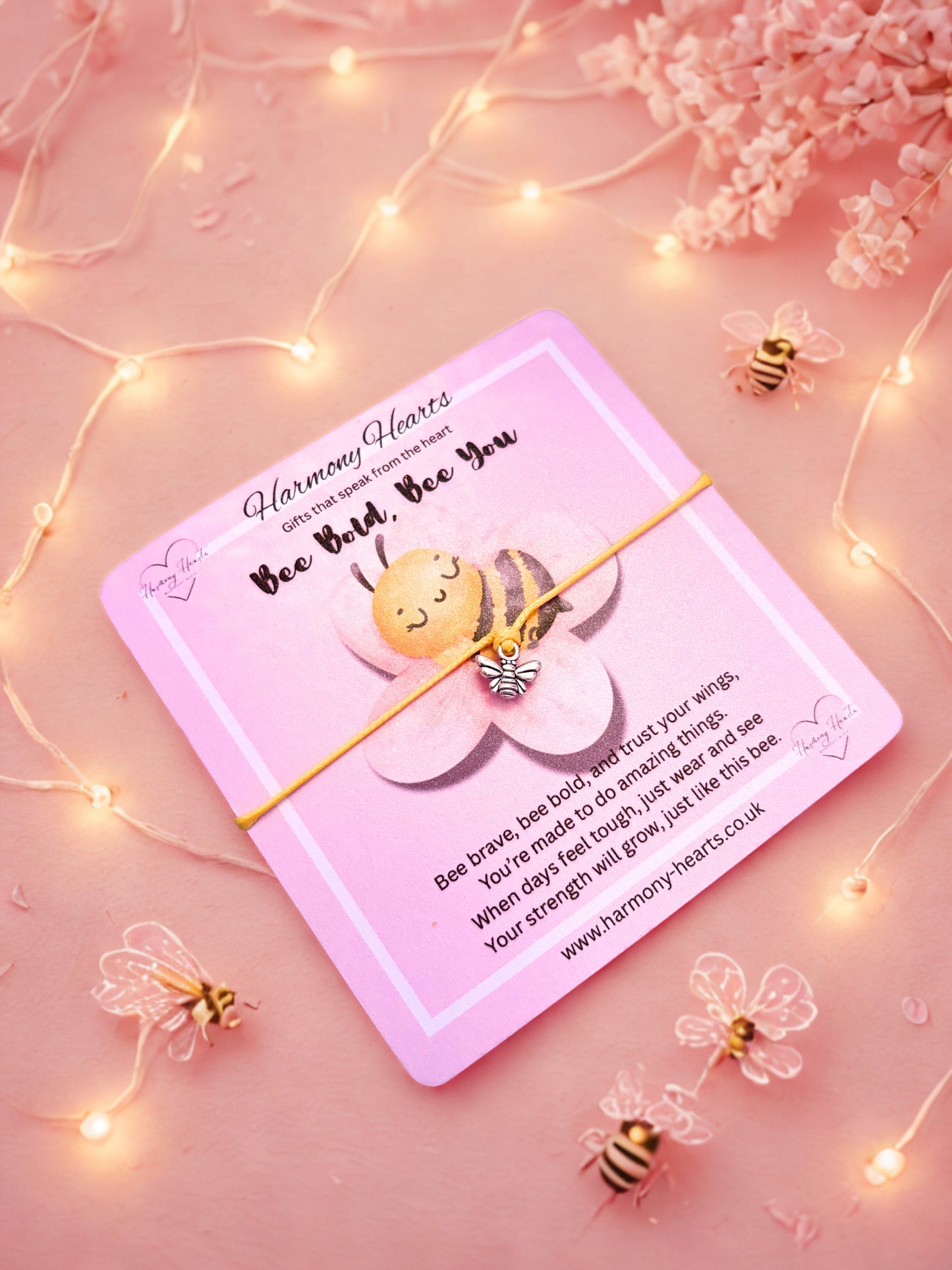 Bee Bracelet on a Pink card with a bee and flower design on a pink background with fairy lights and flowers.