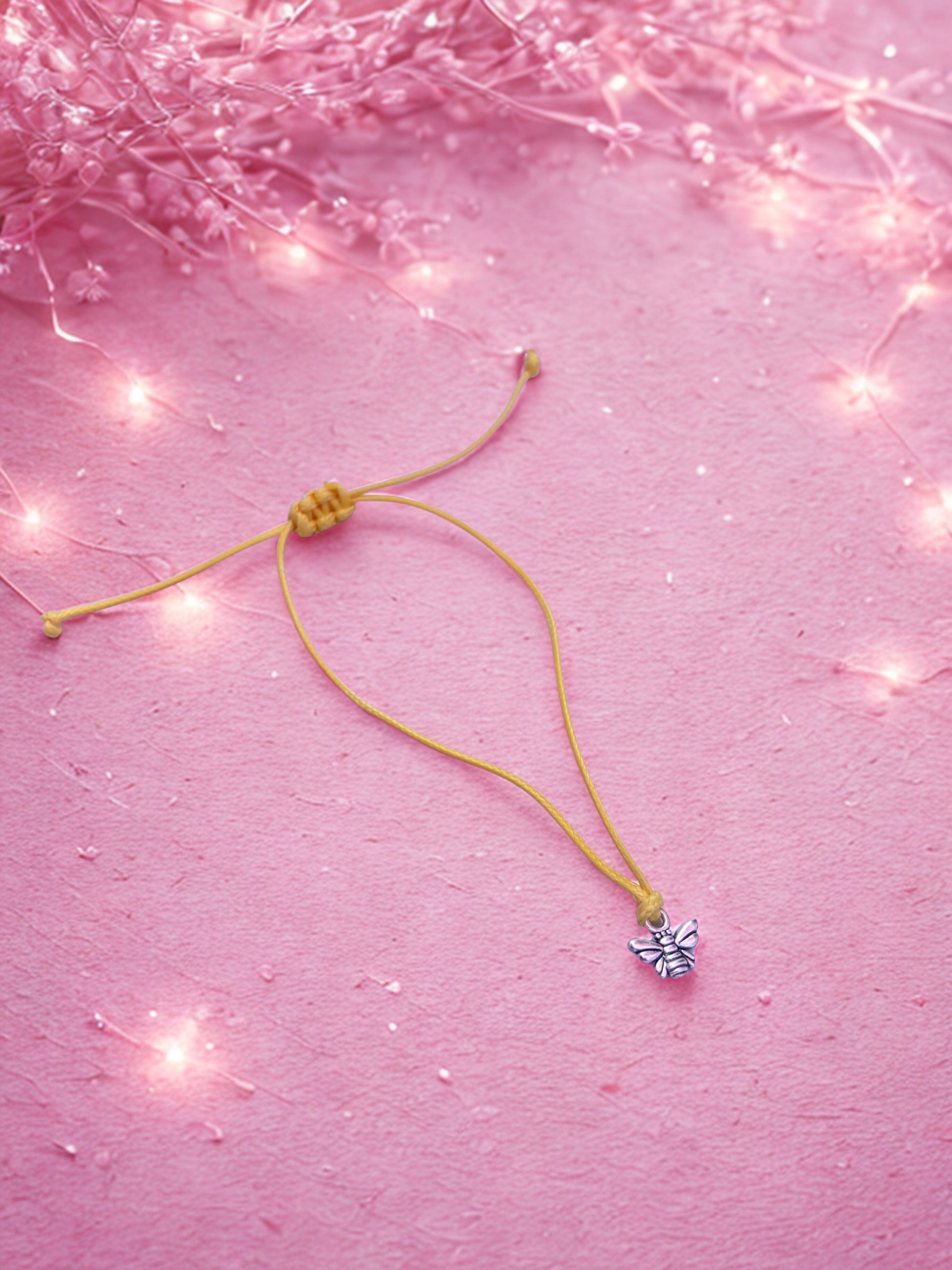 Yellow bracelet with a bee charm on a pink background with string lights