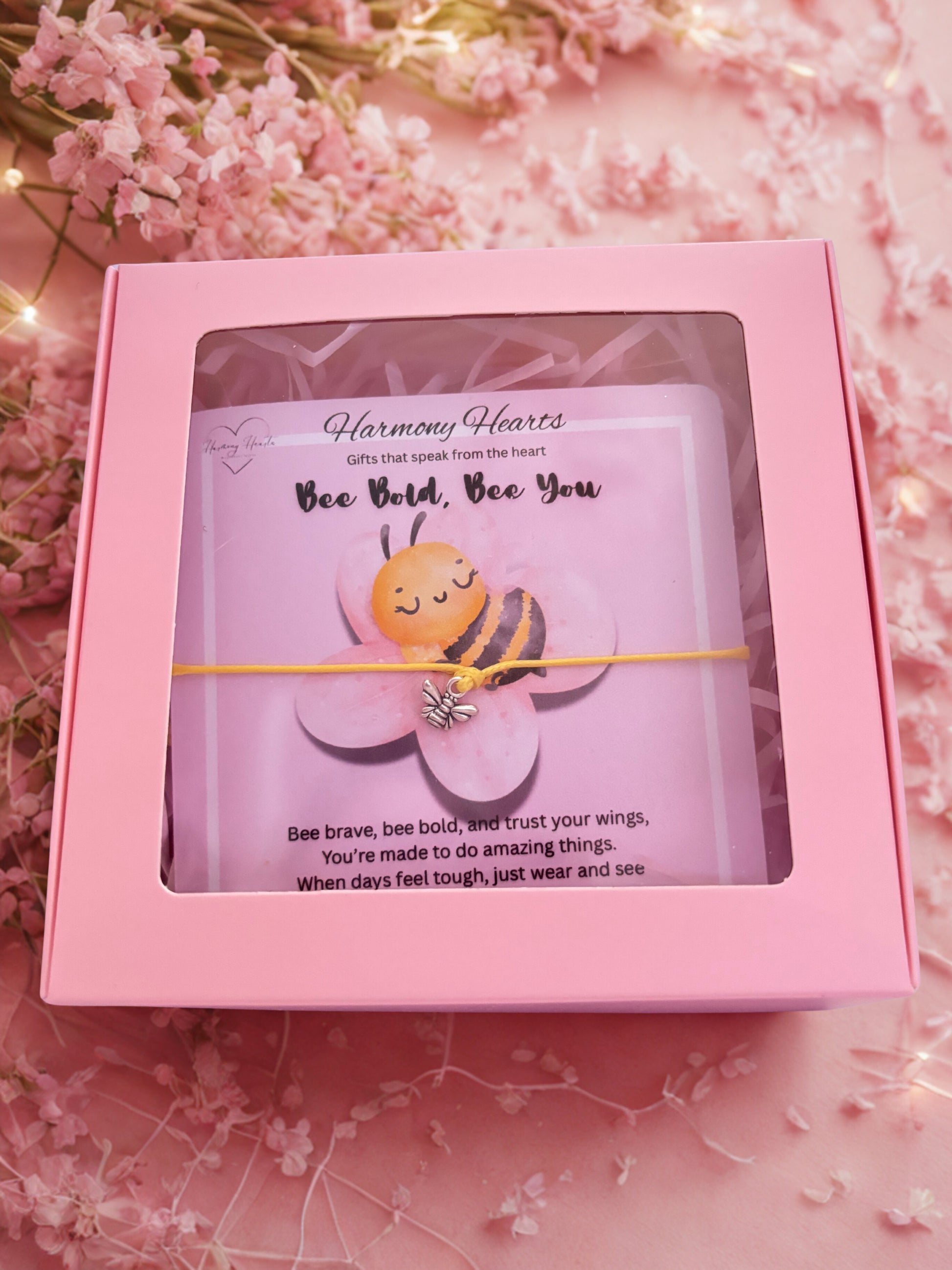 Pink box with a card and yellow string bee bracelet, featuring a bee illustration on a pink floral background.