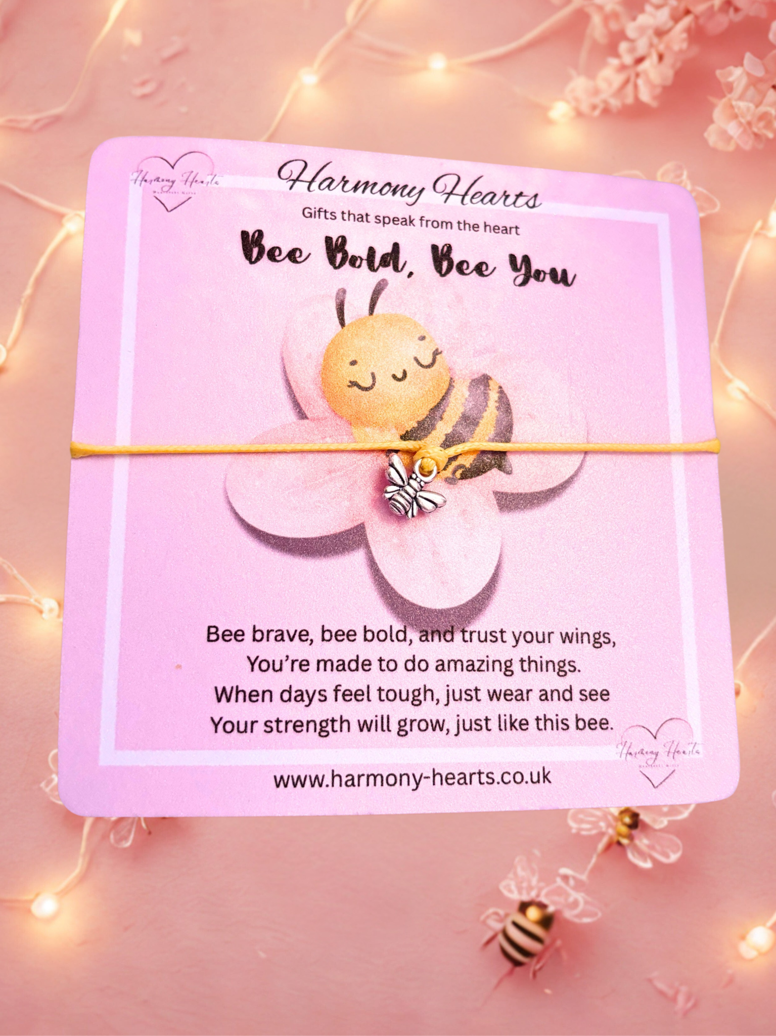 Yellow cord bracelet with silver bee charm on a Pink card with a bee illustration and motivational message on a pink background with fairy lights.