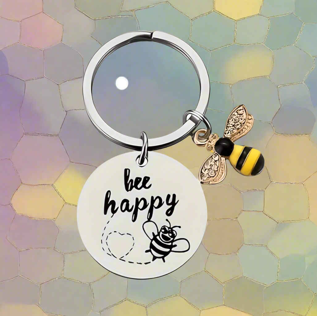 Keychain with 'be happy' tag and bee charm on a colorful hexagonal pattern background