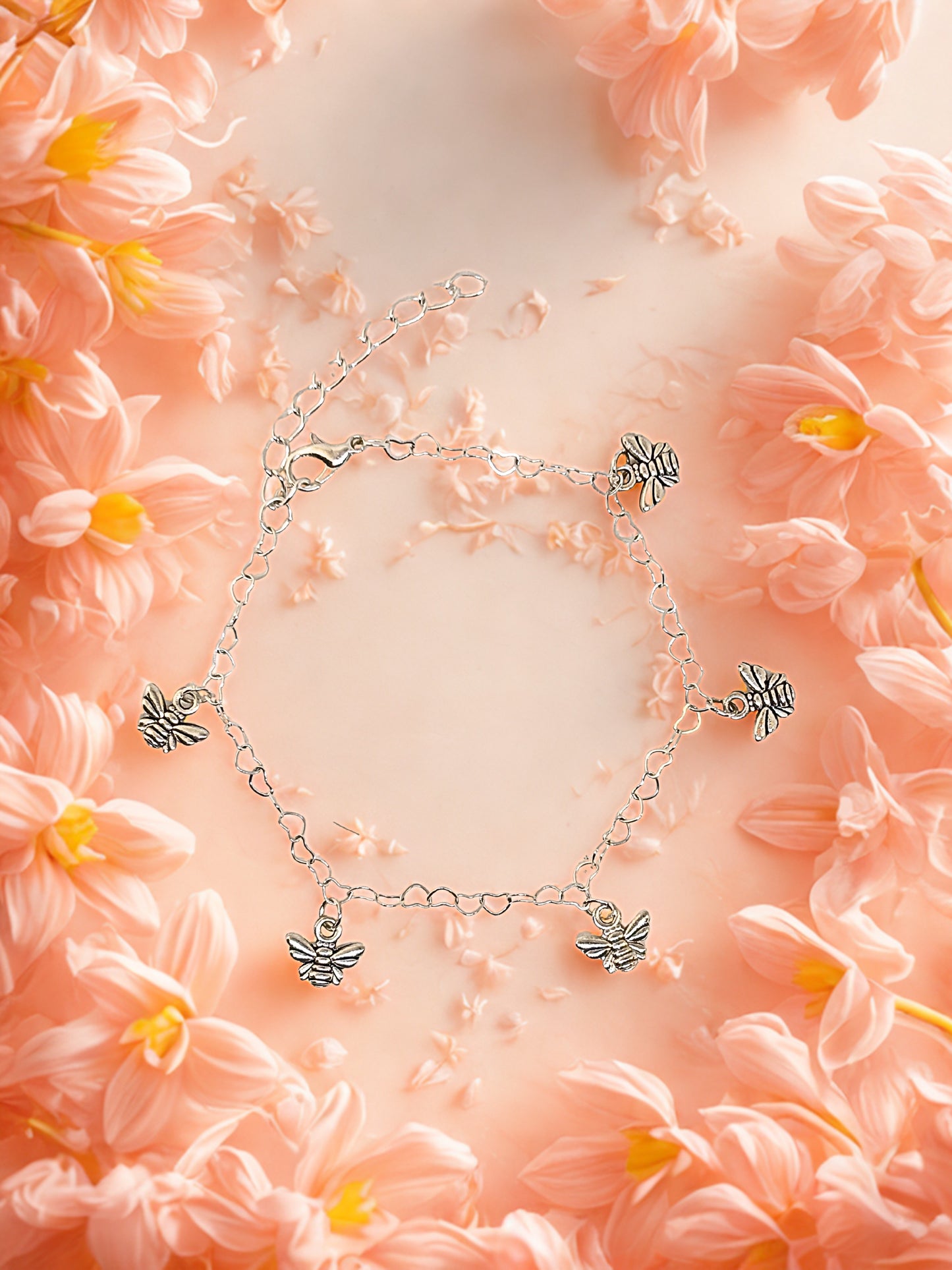 Silver bracelet with bee charms on a pink floral background