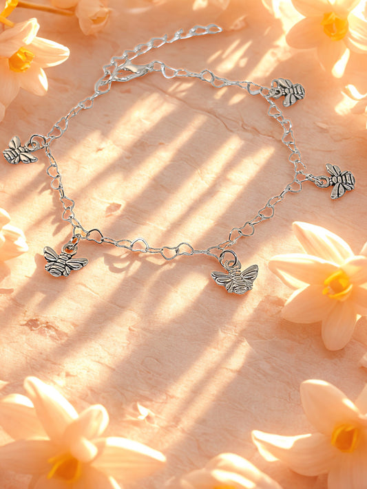 Silver bracelet with bee charms on a wooden surface with flowers