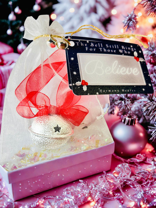 Silver Bell with red ribbon and believe tag under a Christmas tree