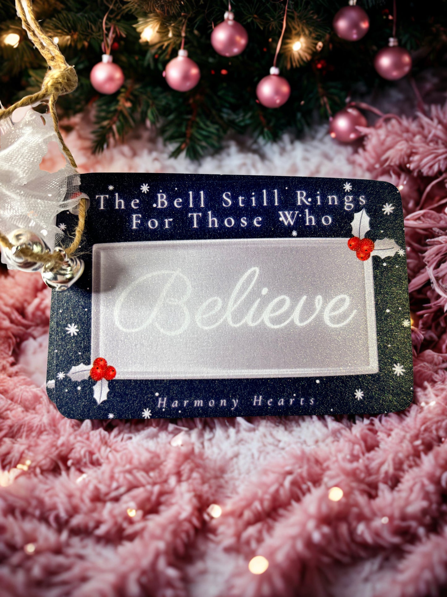 Decorative Christmas tag with text 'The Bell Still Rings For Those Who Believe' on a pink textured background.