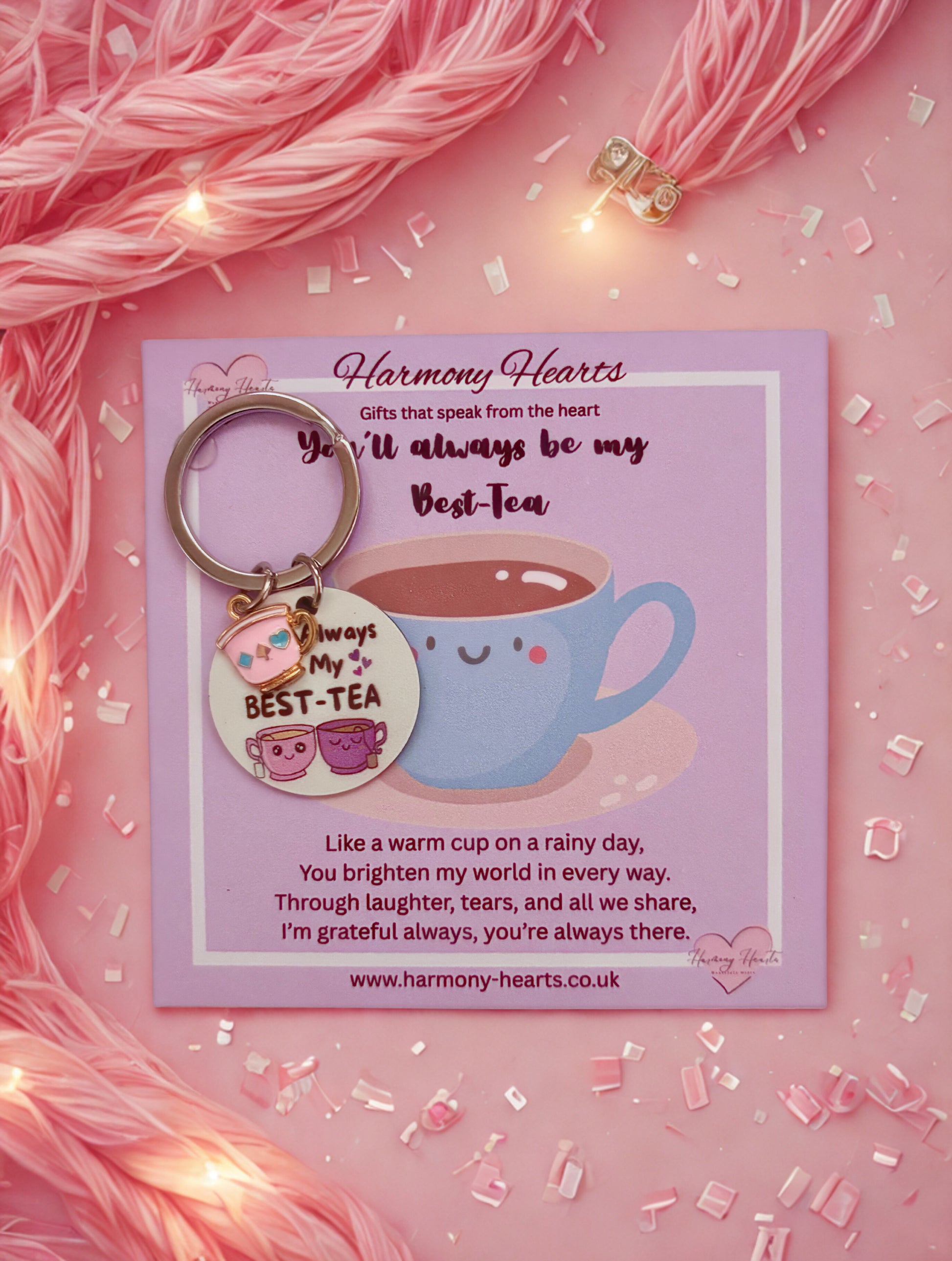 Keychain with a tea cup design on a pink card with text, surrounded by pink yarn and lights.