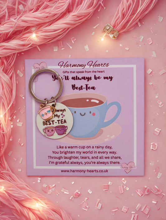 Keychain with a tea cup design on a pink card with text, surrounded by pink yarn and lights.