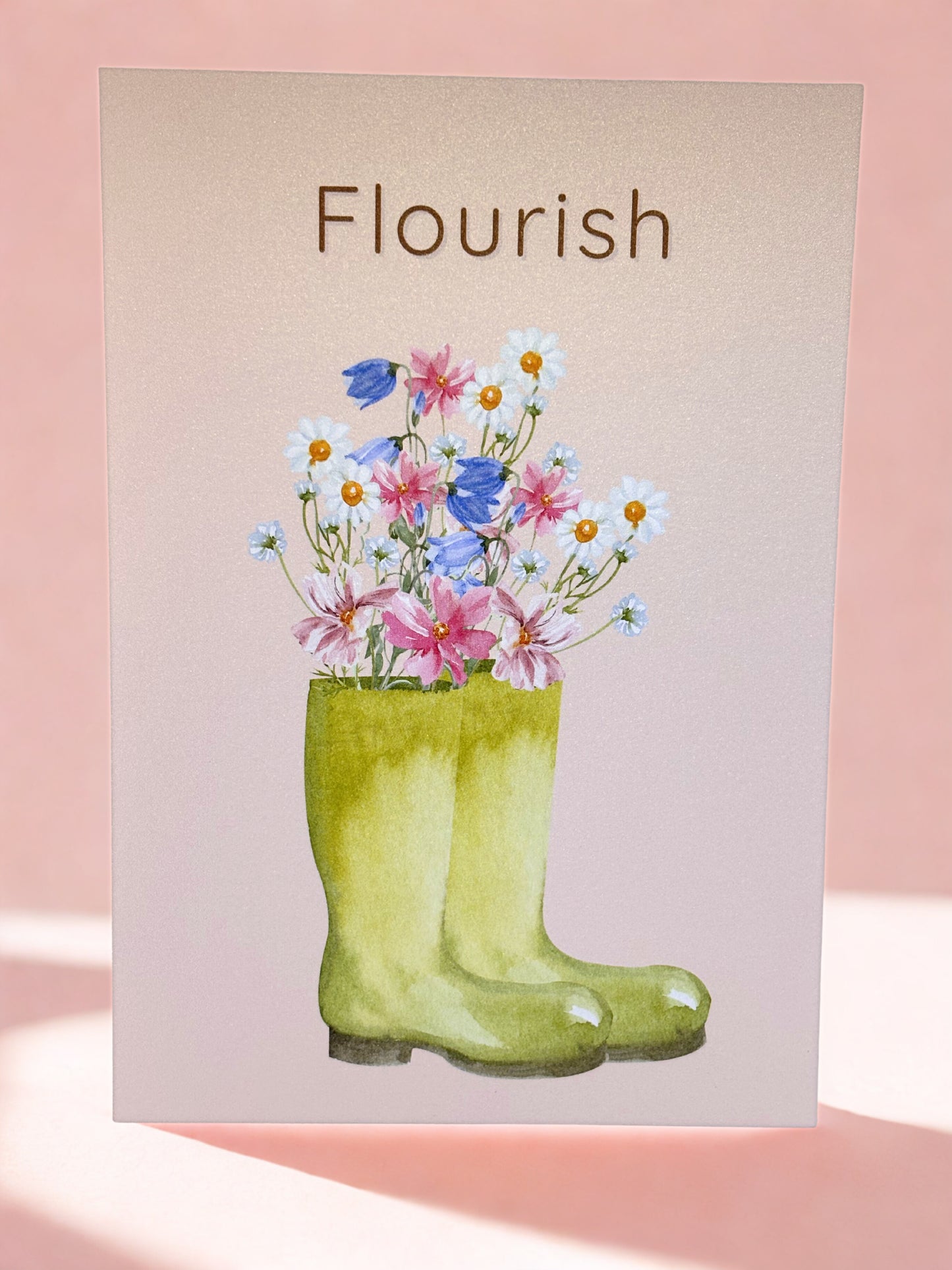 print with green wellington boots holding flowers and 'Flourish' text on a pink background