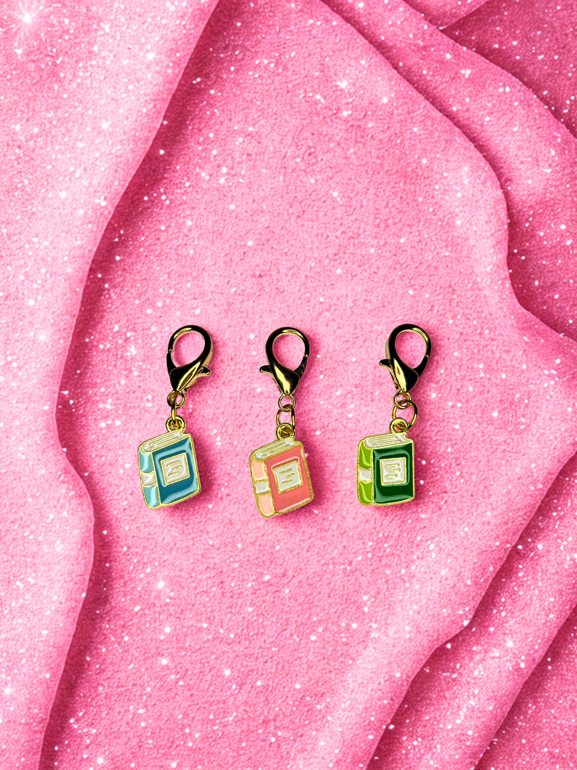 Three colorful square-shaped keychains with clips on a pink textured background