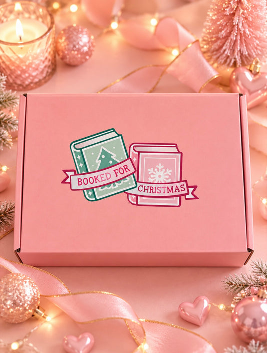 A pink subscription box decorated with a 'Booked For Christmas' illustration, styled on a festive pink background with Christmas ornaments, ribbons, and warm string lights.