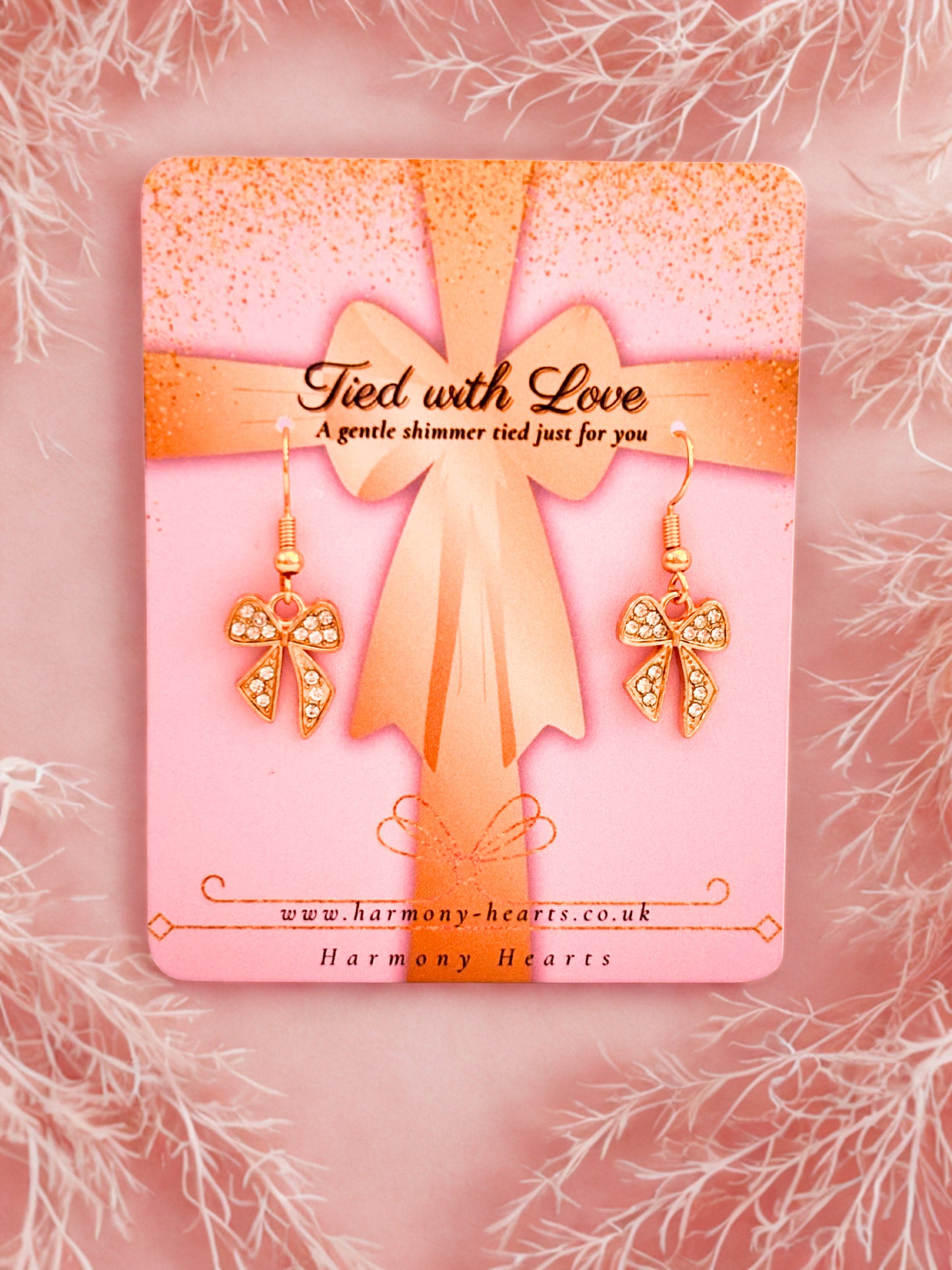 Sparkly gold bow earrings on a pink Harmony Hearts branding card