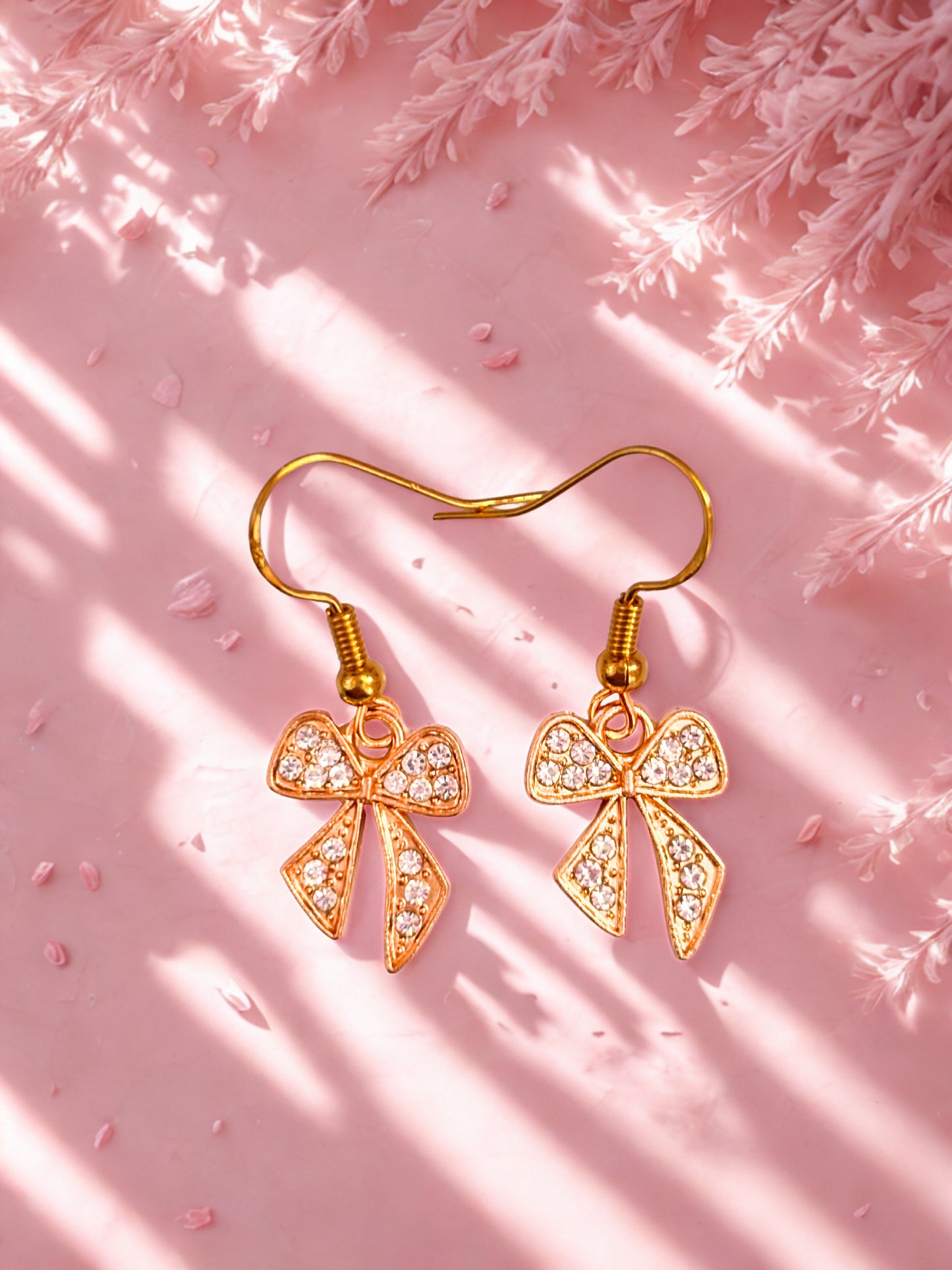 Gold sparkly bow shaped earrings against a pink background