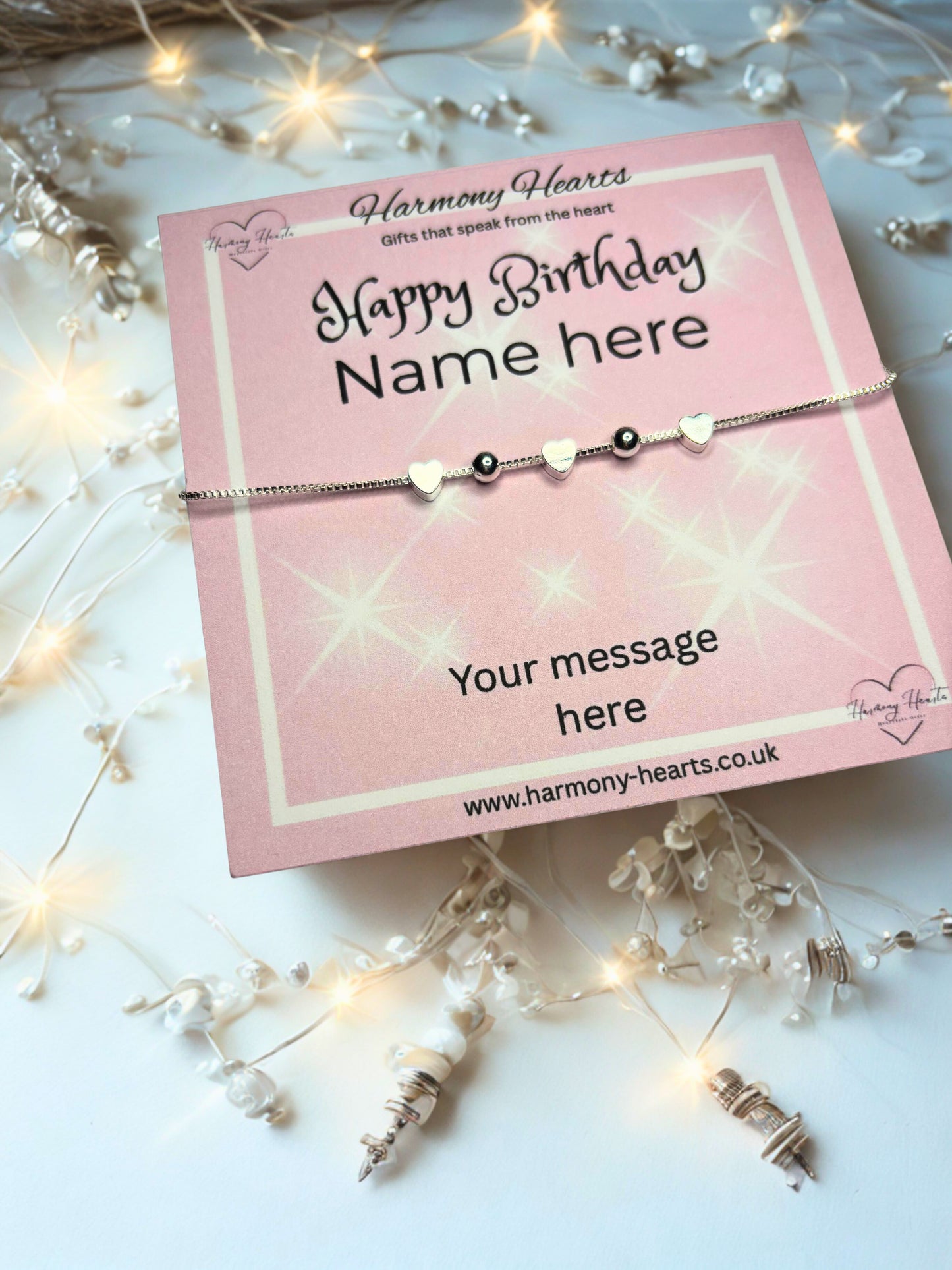 Bracelet on a pink card with 'Happy Birthday' message, surrounded by decorative lights and flowers.