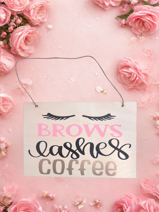 Decorative sign with 'Brows Lashes Coffee' text on a pink floral background