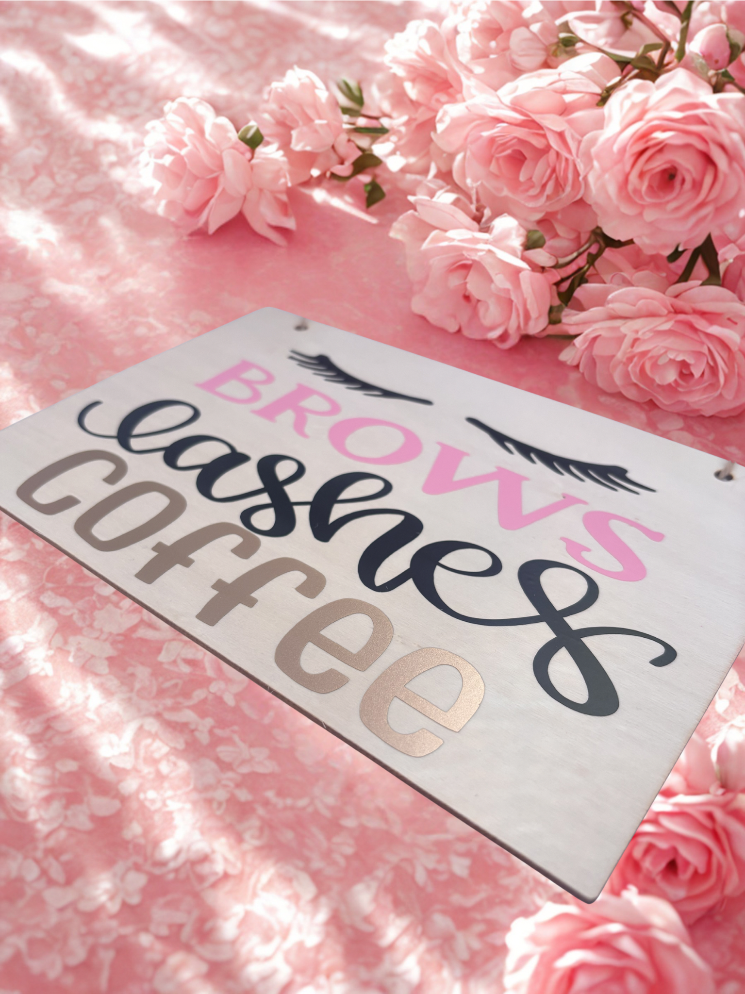 Decorative sign with 'Brows Lashes Coffee' text on a pink floral background