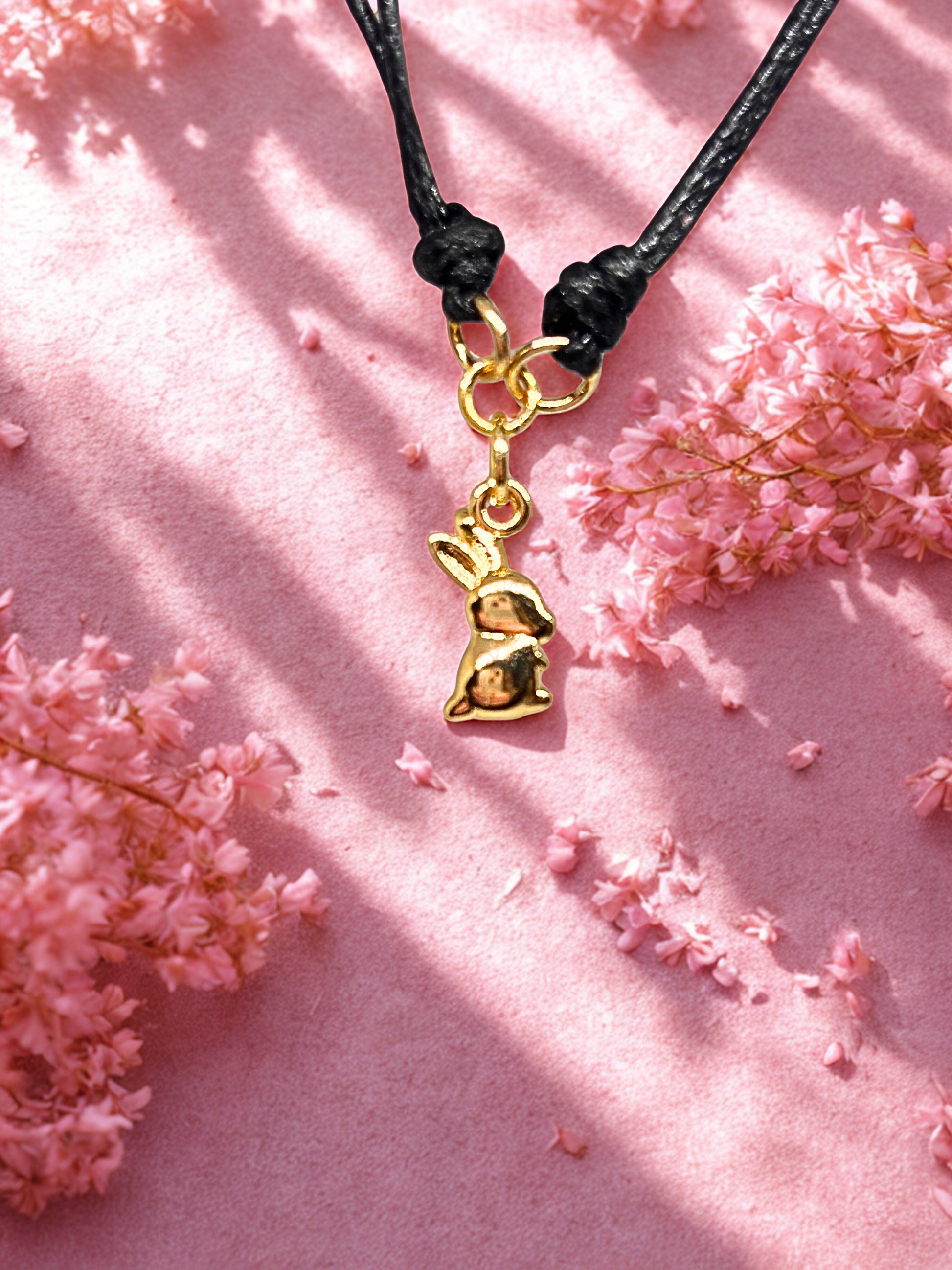 Gold bunny charm on a black cord against a pink floral background