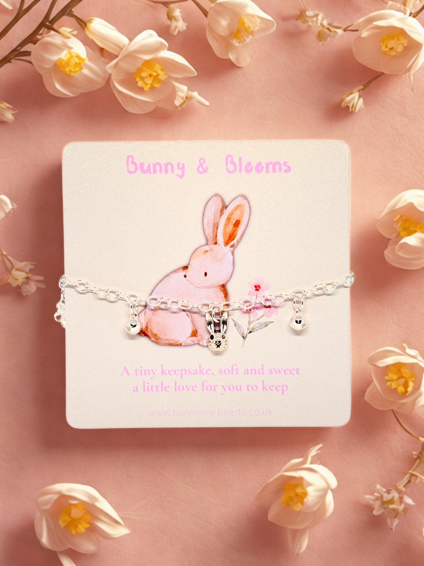 Bracelet with a bunny charm on a card labeled 'Bunny & Blooms' surrounded by white flowers on a pink background.