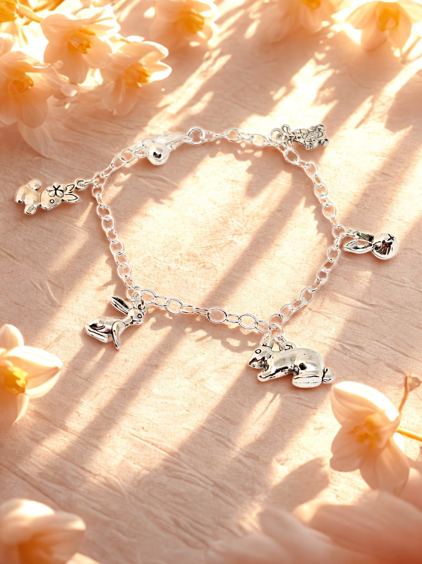 Silver bracelet with bunny charms on a soft peach-colored background with flowers