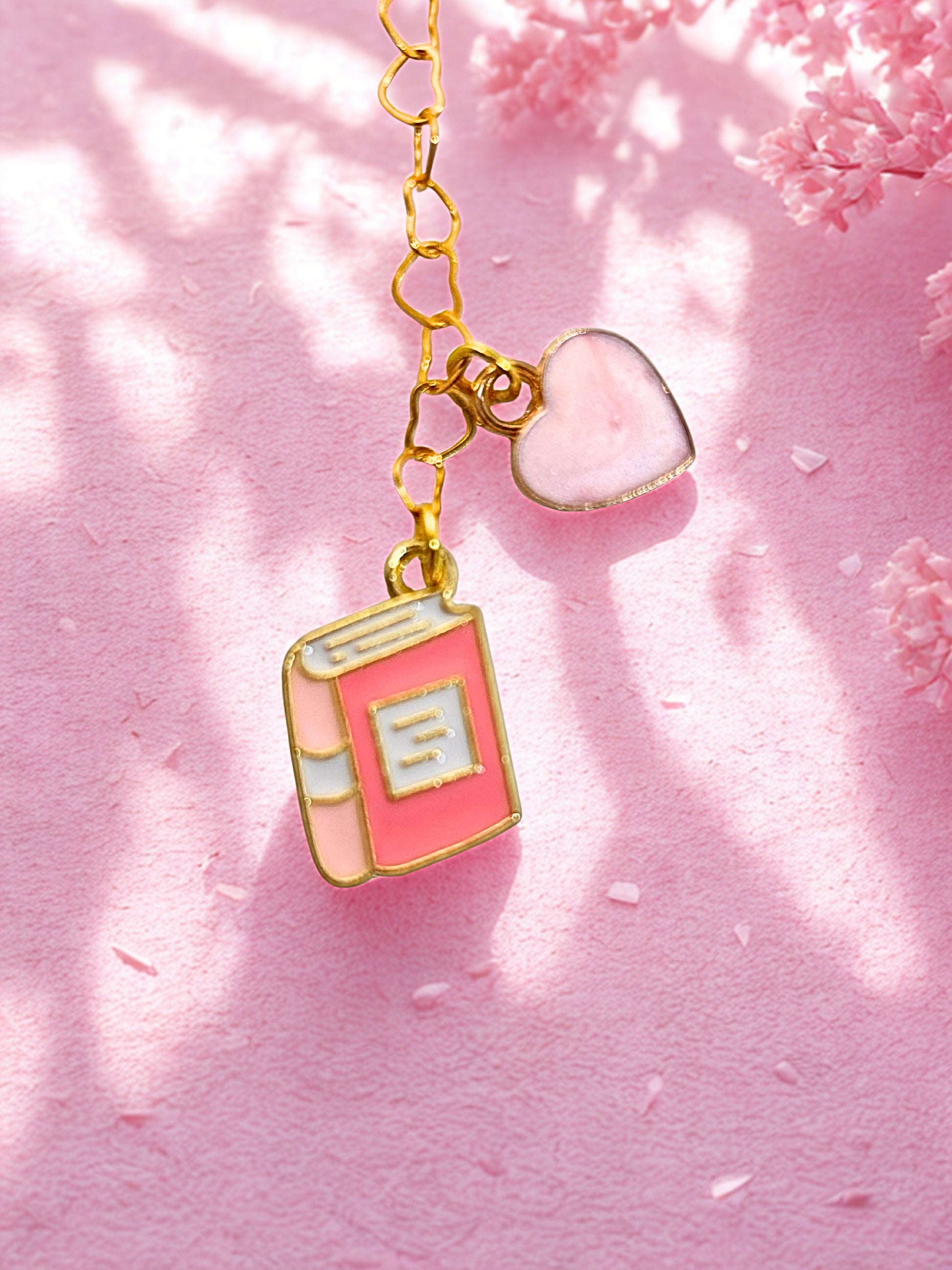 Pink book-shaped charm on a chain with a heart pendant against a pink background