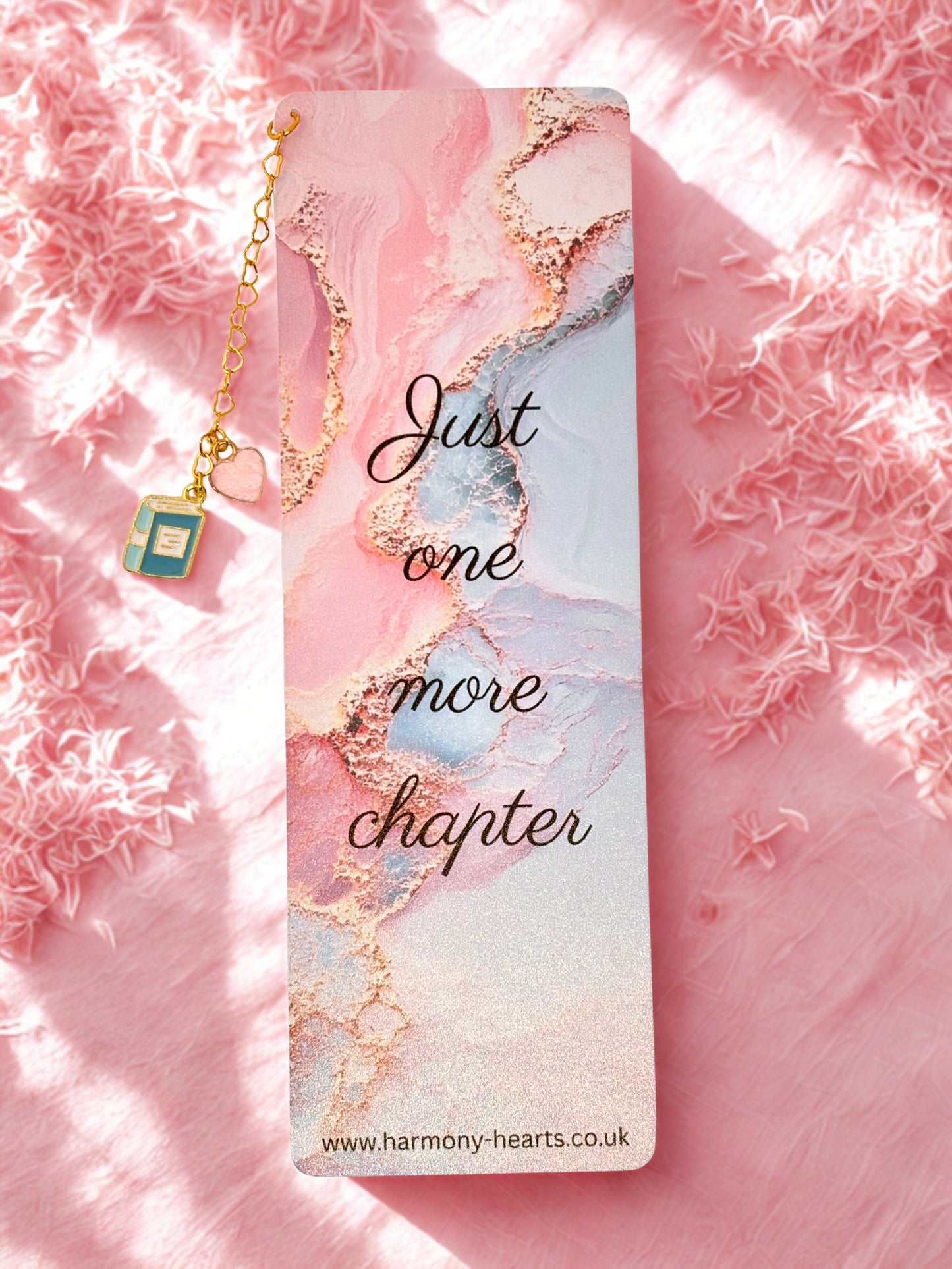 Bookmark with 'Just one more chapter' text on a pink and gold marbled background with a necklace.