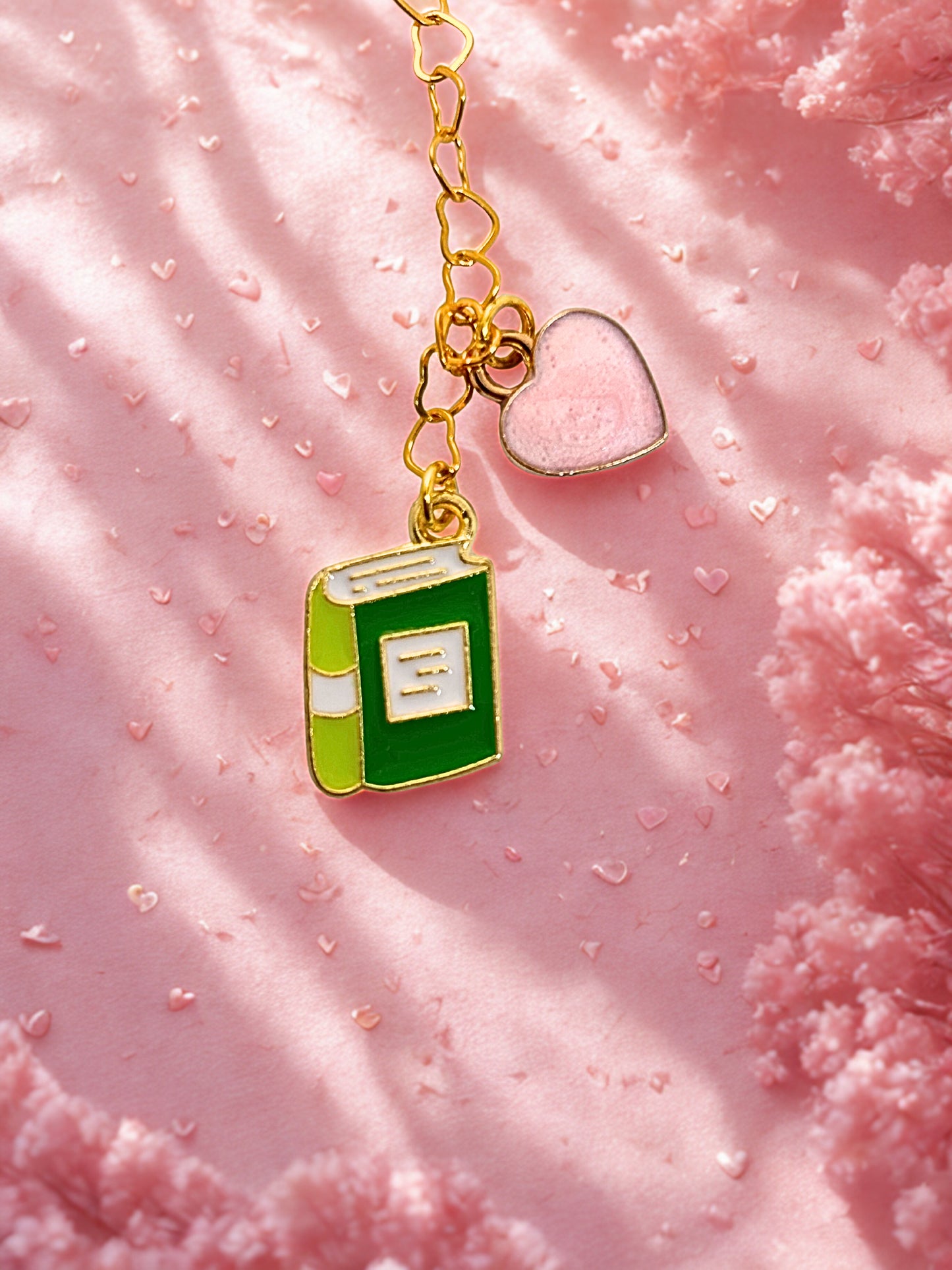 Green book-shaped charm with a gold chain on a pink textured background