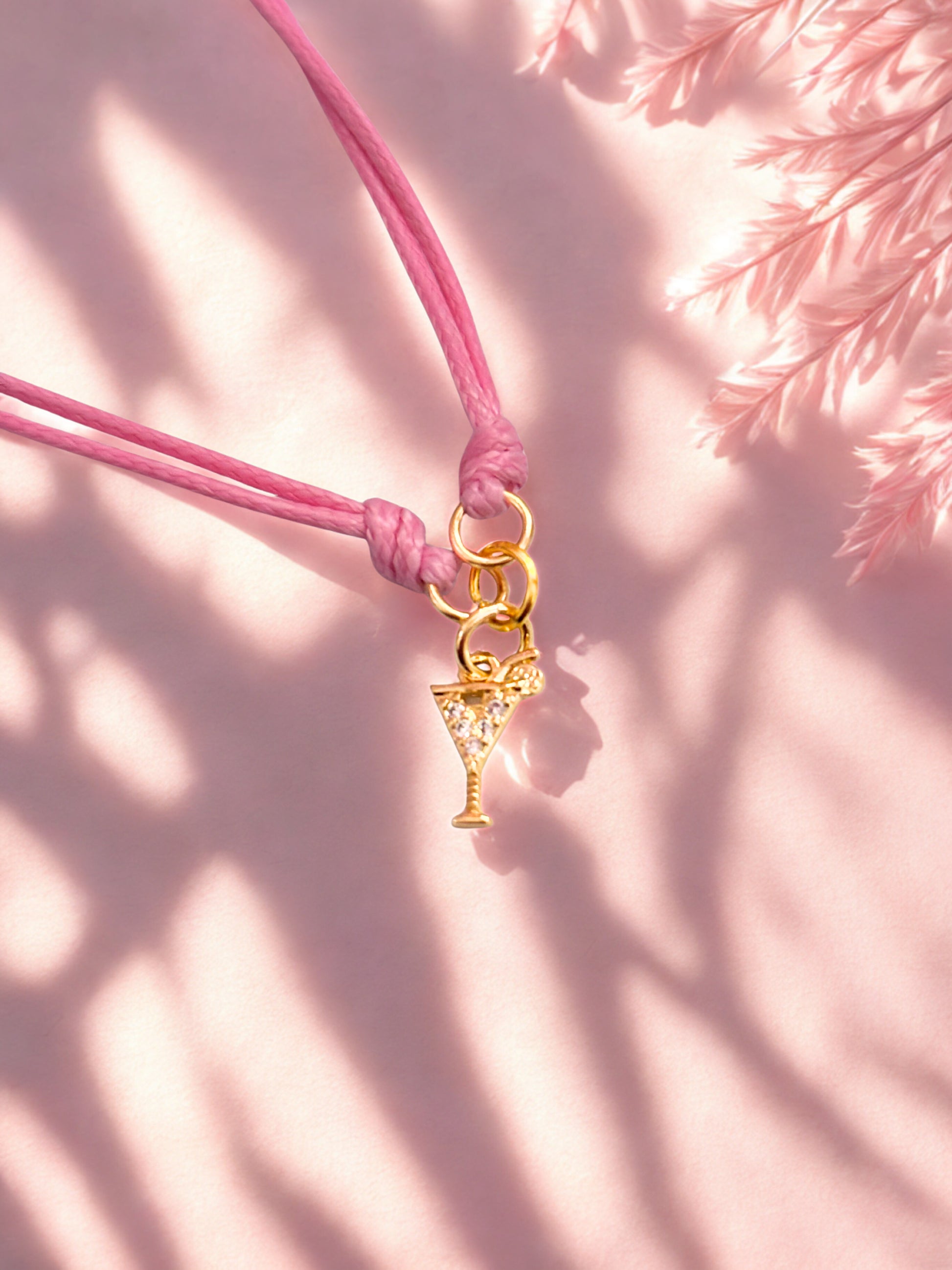Pink cord bracelet with a gold cocktail charm on a pink background