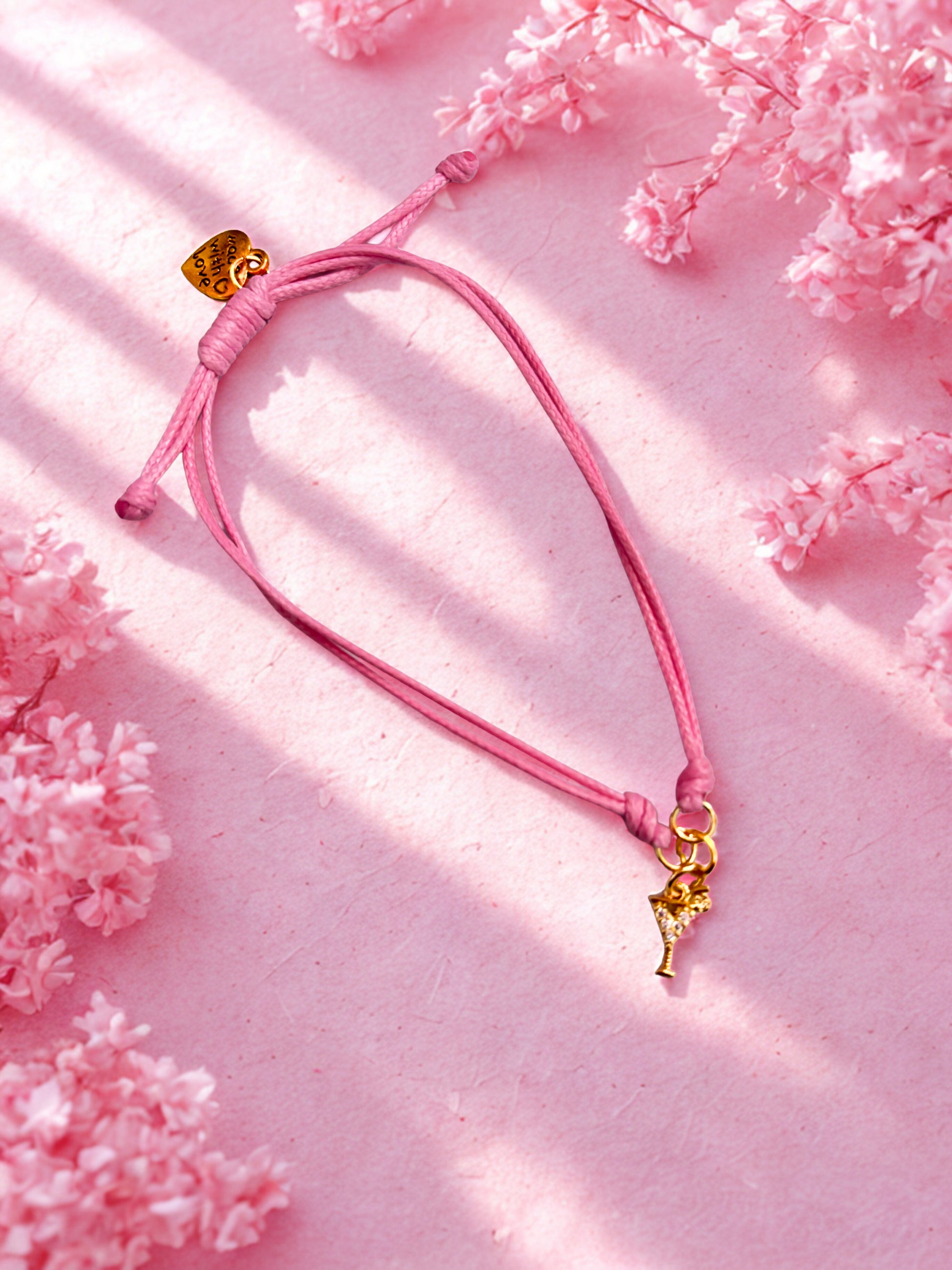 Pink bracelet with a gold cocktail charm on a pink floral background