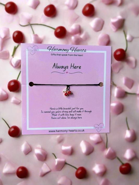Bracelet with cherry charm on a pink card surrounded by cherries and hearts