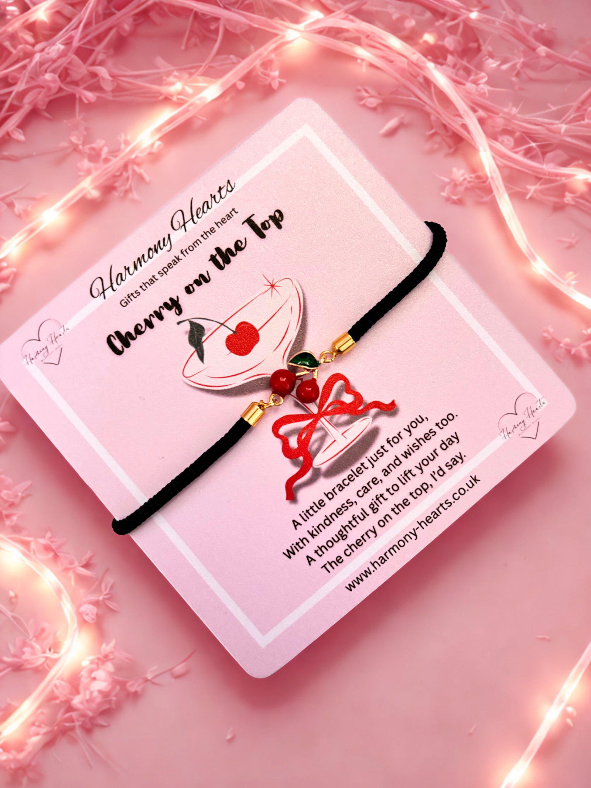 Bracelet with cherry design on a pink card with decorative lights and flowers.