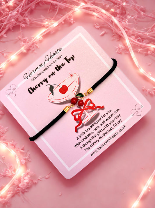 Bracelet with cherry design on a pink card with decorative lights and flowers.