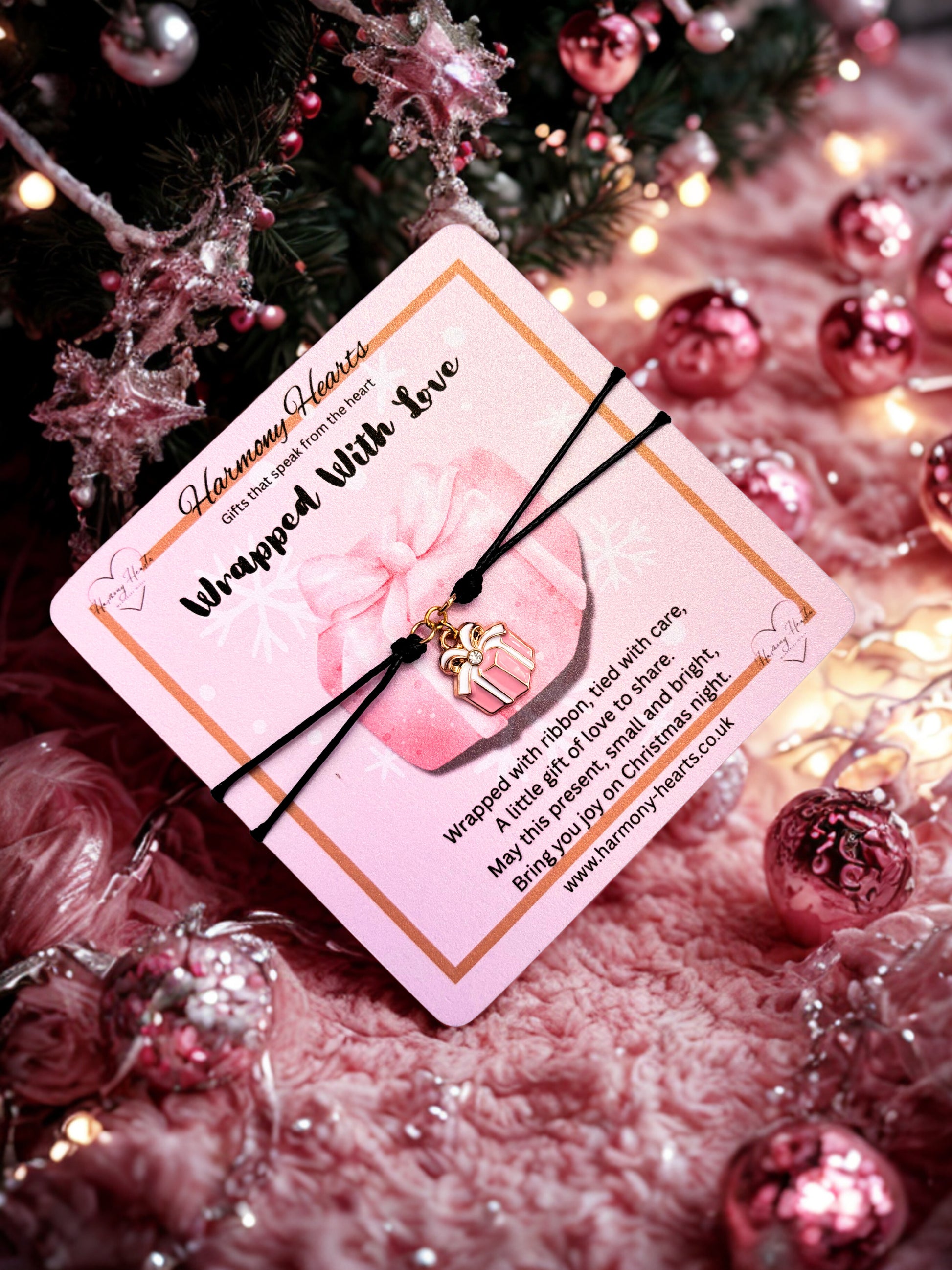 Bracelet with pink card and gold present charm on a festive background with Christmas decorations.