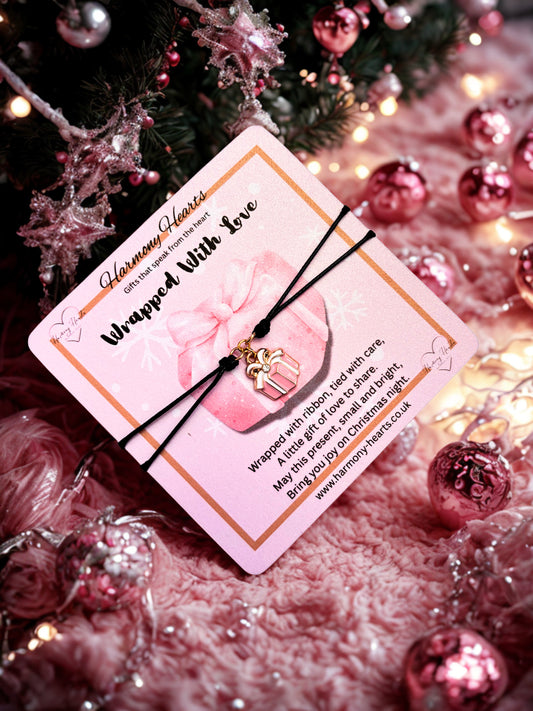 Bracelet with pink card and gold present charm on a festive background with Christmas decorations.