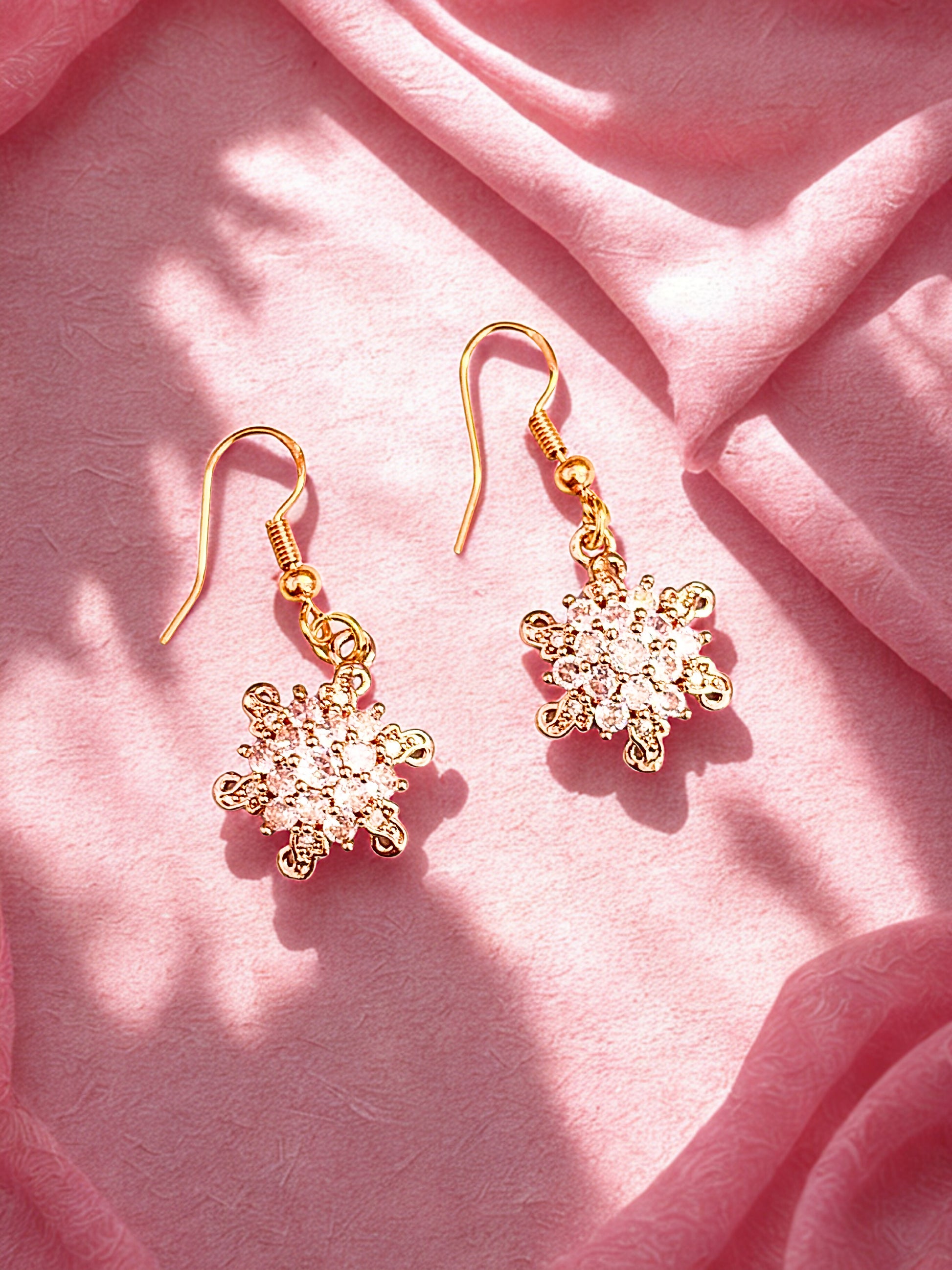 Gold snowflake earrings on a pink fabric background