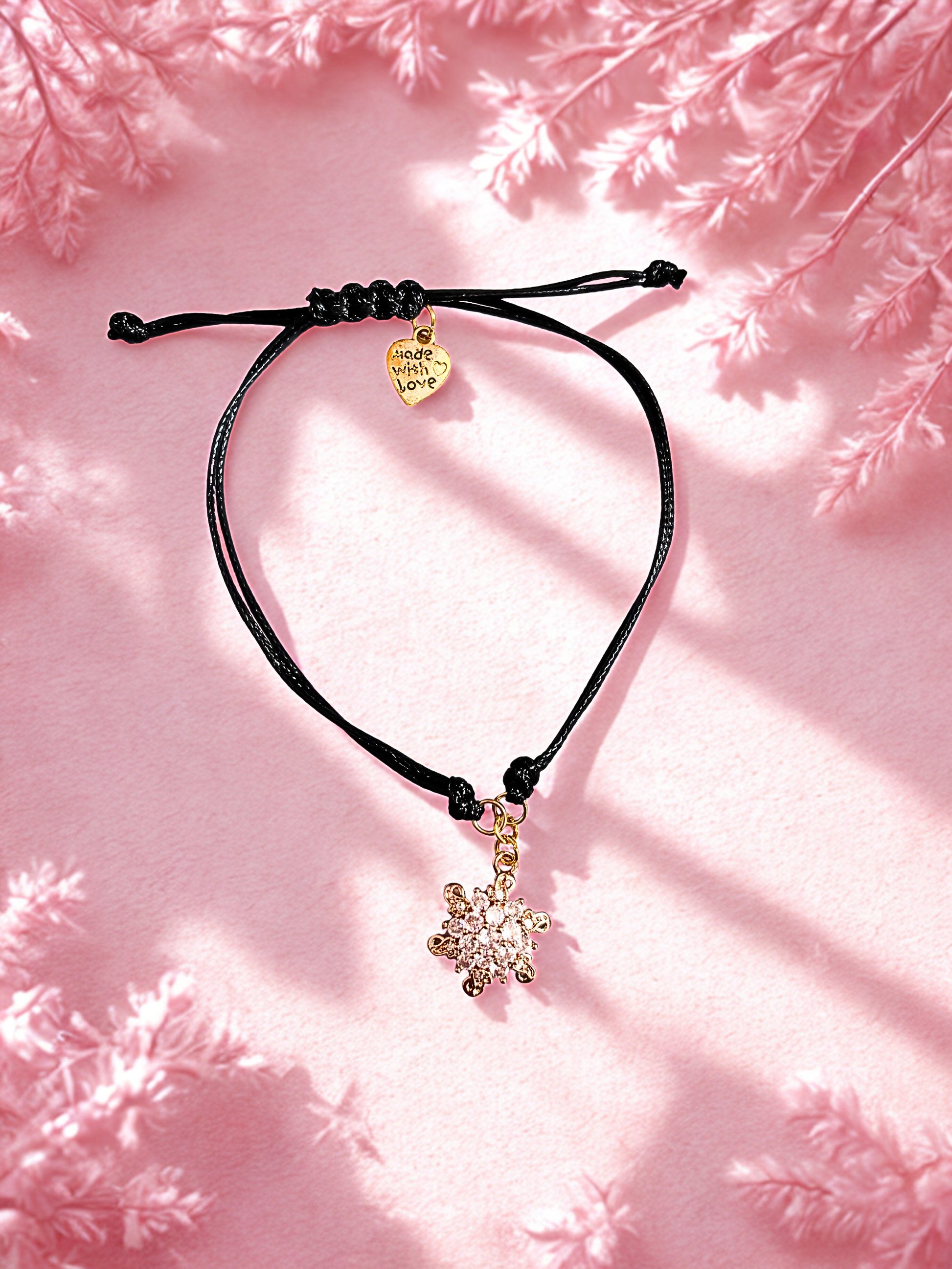 Black cord bracelet with heart and snowflake charms on a pink textured background