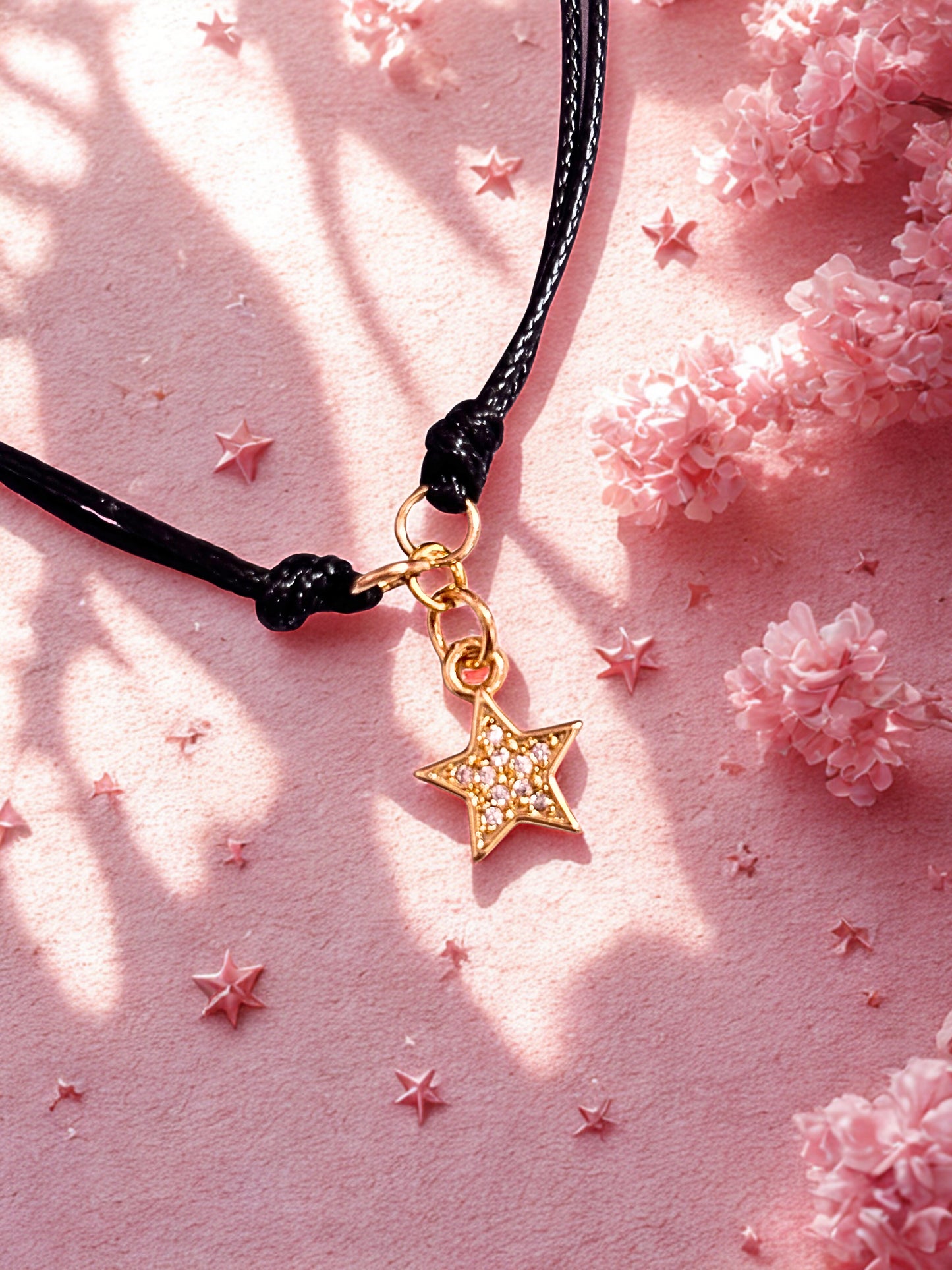 Gold star charm on a black cord bracelet on a pink background