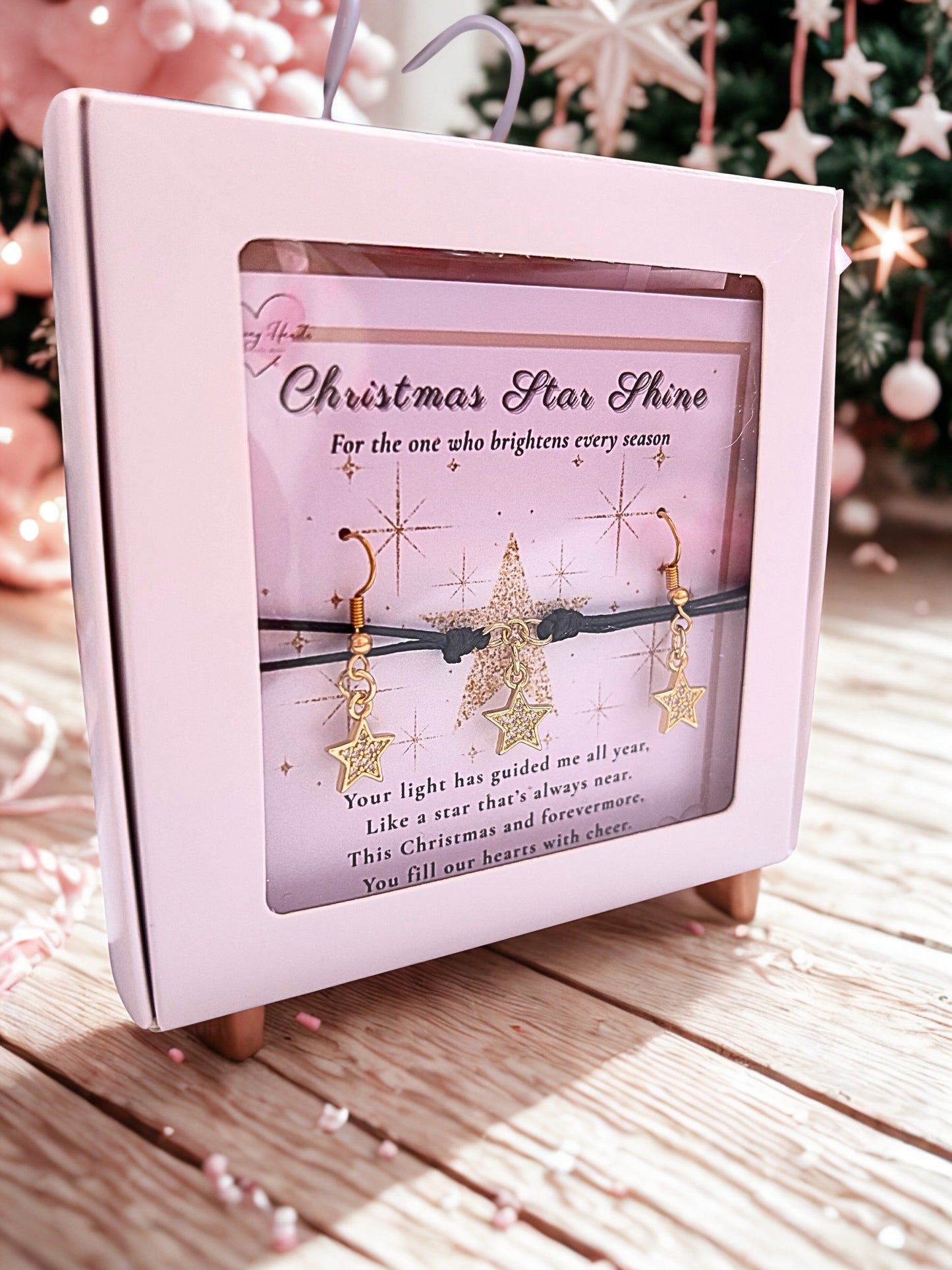 Pink gift box with Christmas-themed earrings and decorative text against a festive background.