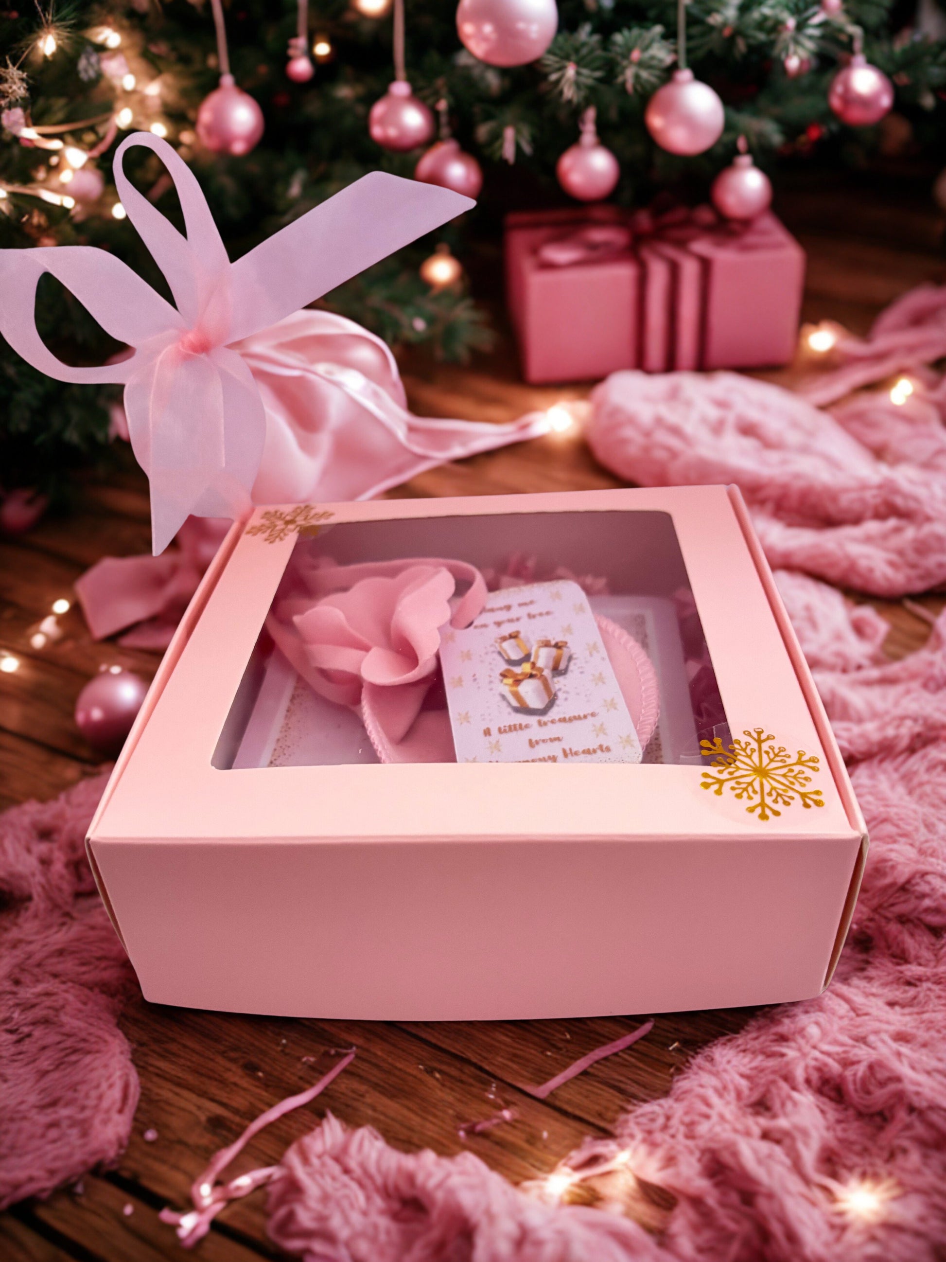 Pink gift box with a bow, and a card inside, set against a festive background with Christmas decorations.