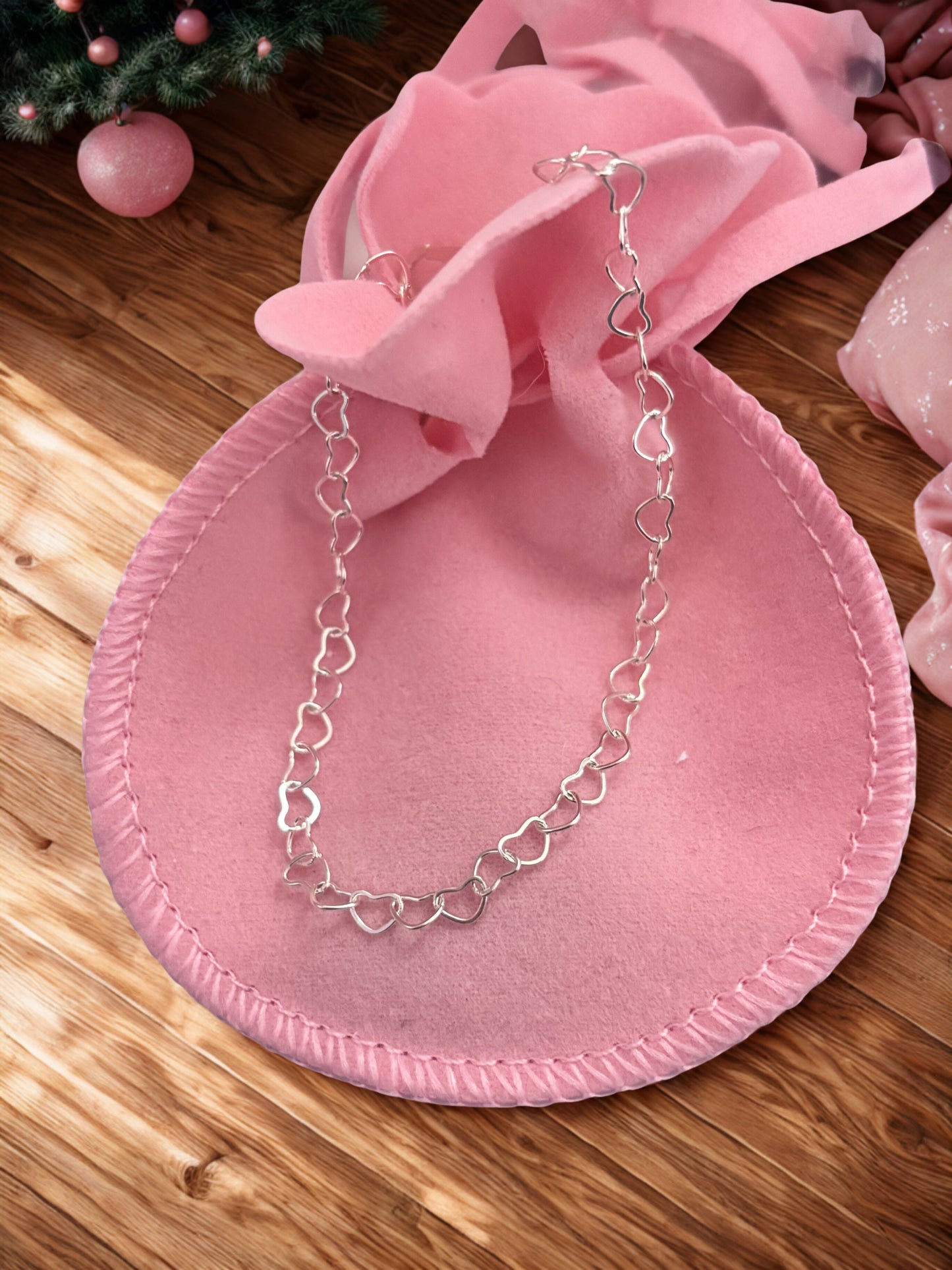 Silver heart-shaped chain bracelet on a pink velvet pouch with a wooden surface background.
