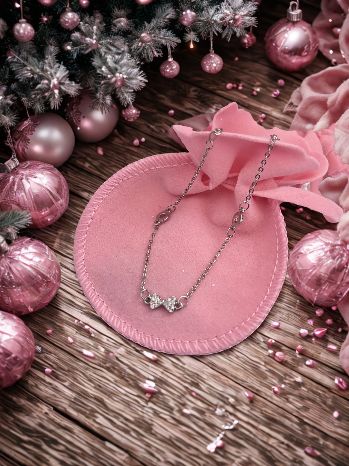 Silver tone bracelet with a bow pendant on a pink velvet pillow surrounded by pink ornaments and flowers.