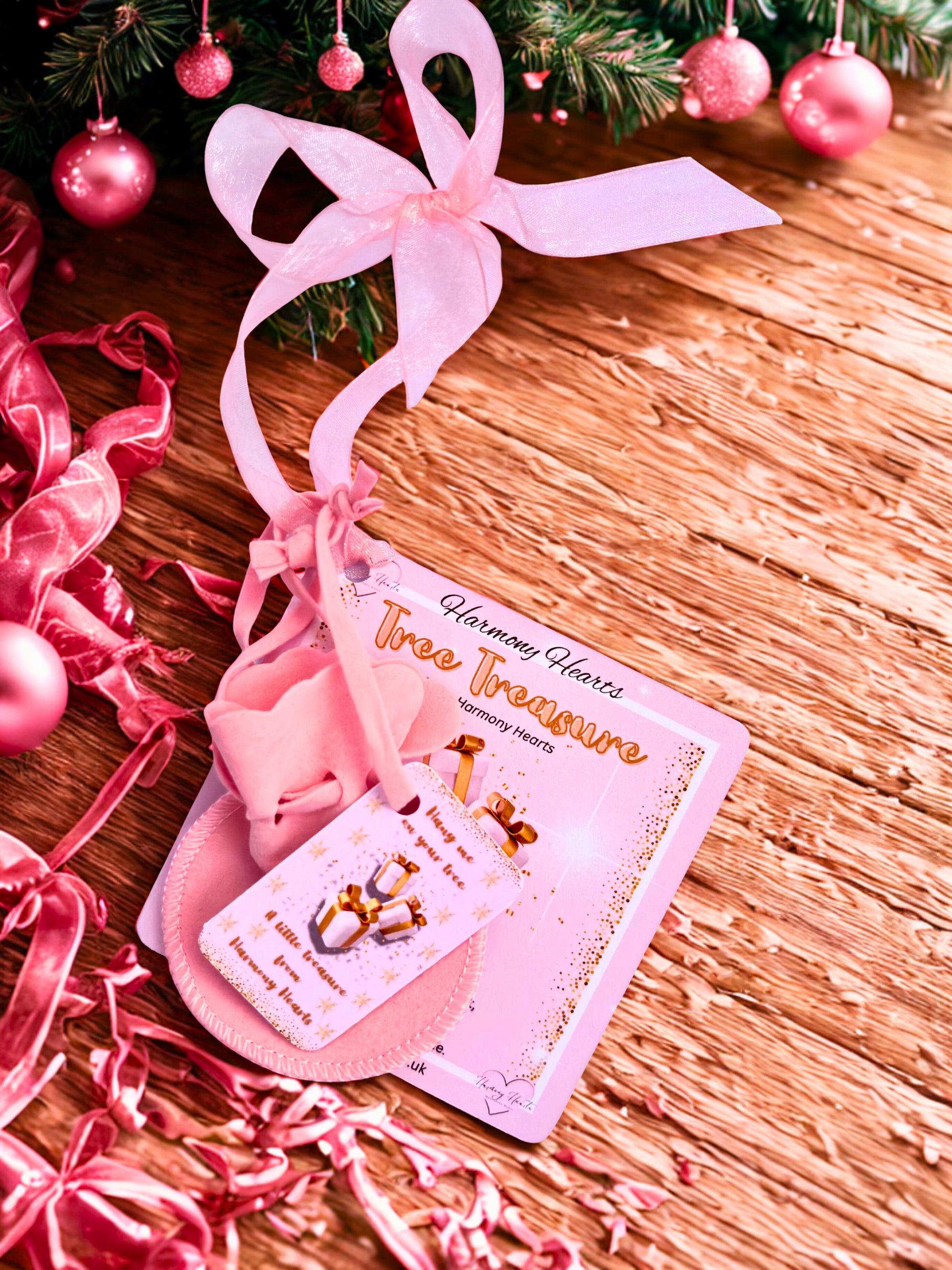 Pink decorative item with a card on a wooden surface with Christmas tree decorations.