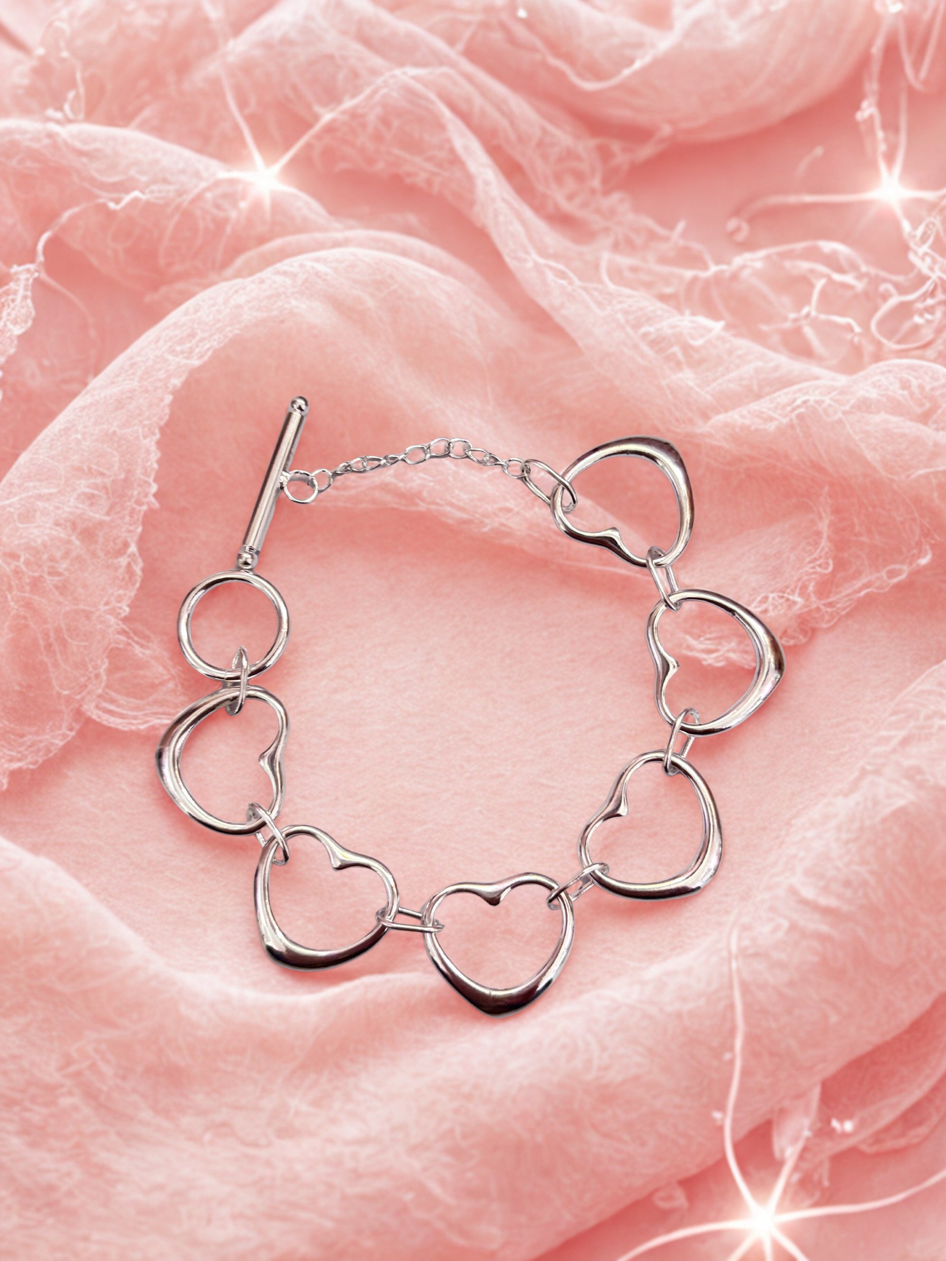 Silver heart-shaped bracelet on a pink fabric background