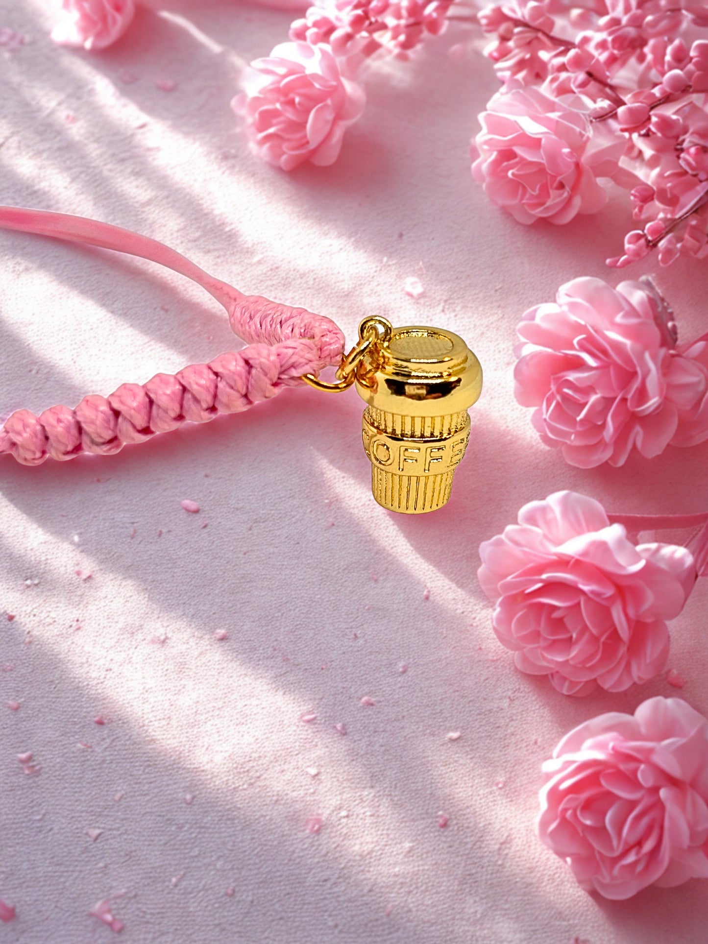 Gold coffee cup charm on a pink cord  bracelet with pink flowers in the background