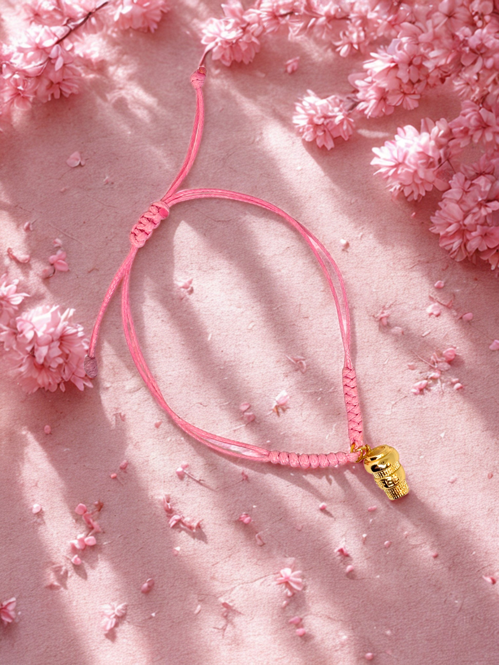 Pink braided bracelet with a gold coffee cup charm on a pink floral background