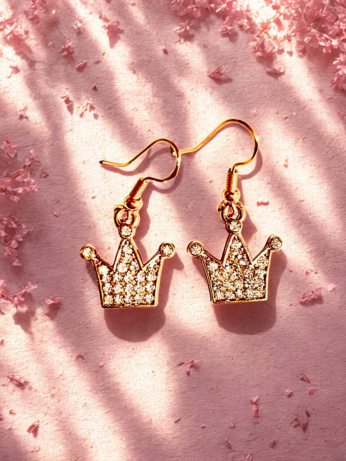 Gold crown-shaped earrings on a pink textured background
