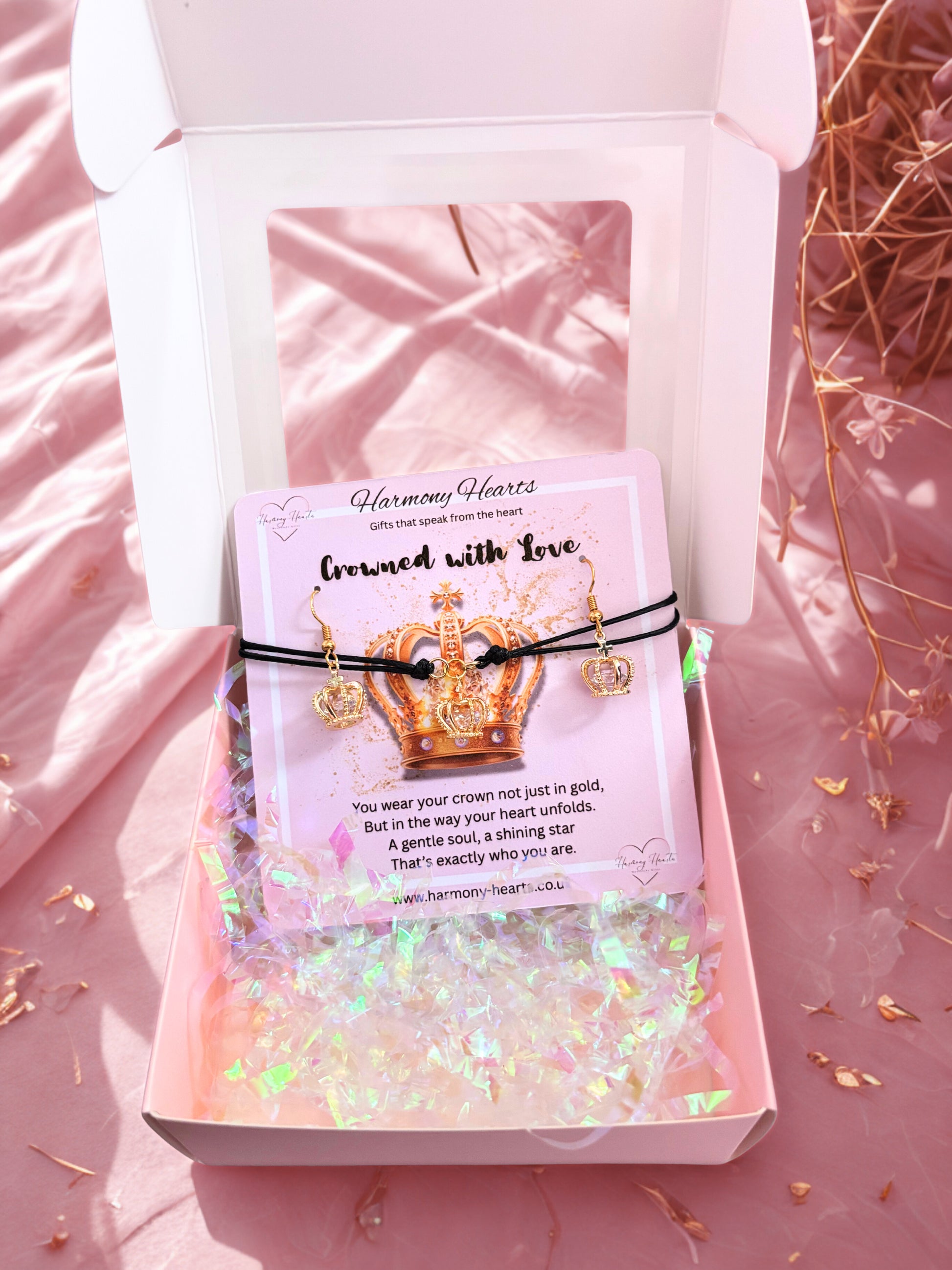 Gold crown earrings and bracelet with a card in a decorative box on a pink surface.
