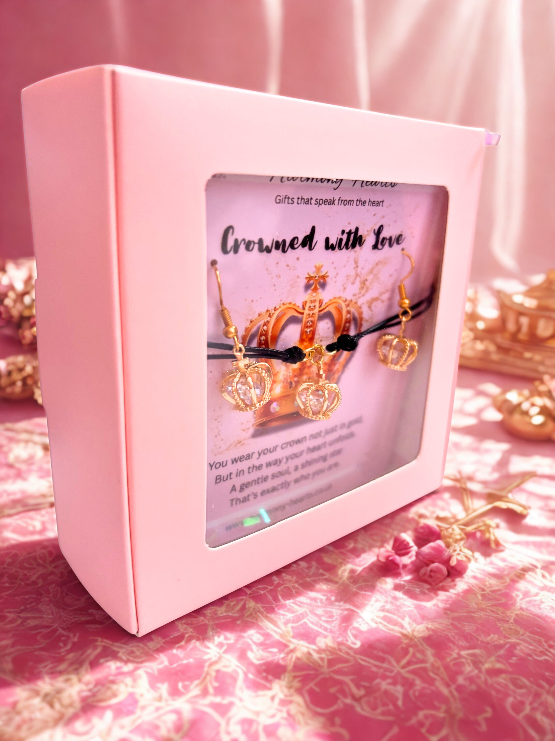 Pink jewelry box with a display of gold crown bracelet and earrings on a pink fabric background