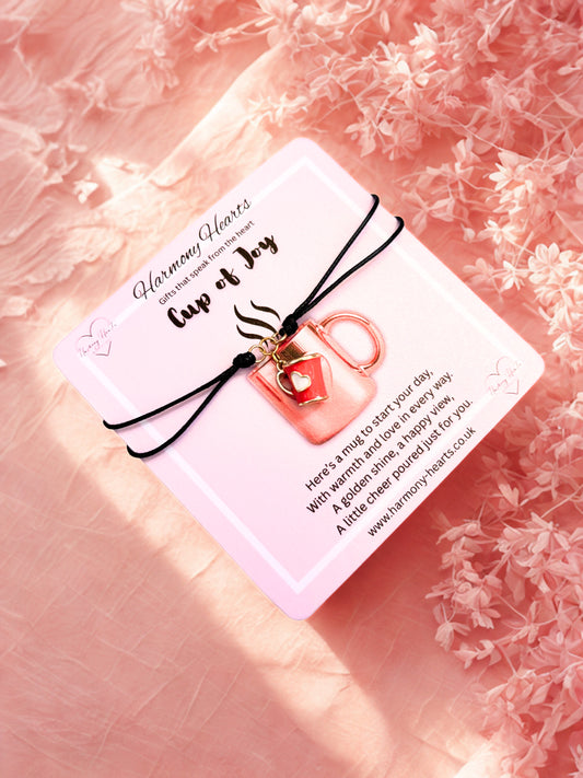 Bracelet with a red mug charm with gold handle on a pink card with text, against a pink floral background