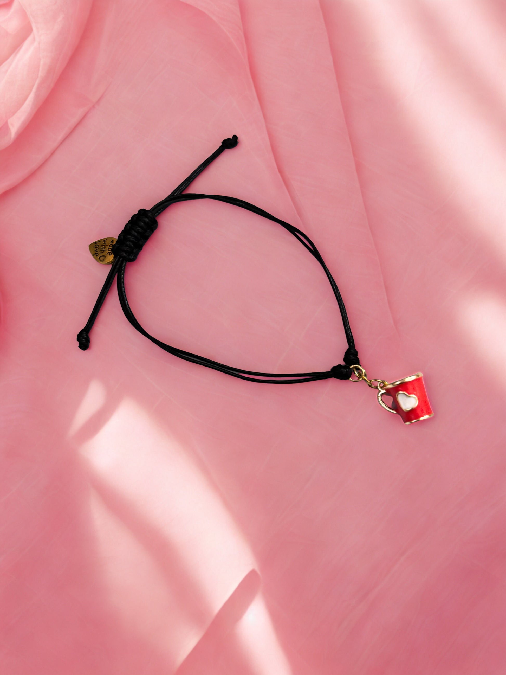 Black cord bracelet with a red cup charm on a pink fabric background